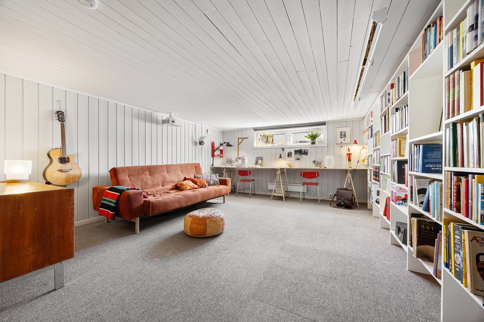 Stor kjellerstue med vegg til vegg-teppe og panel på vegger og i himling. Galleribilde