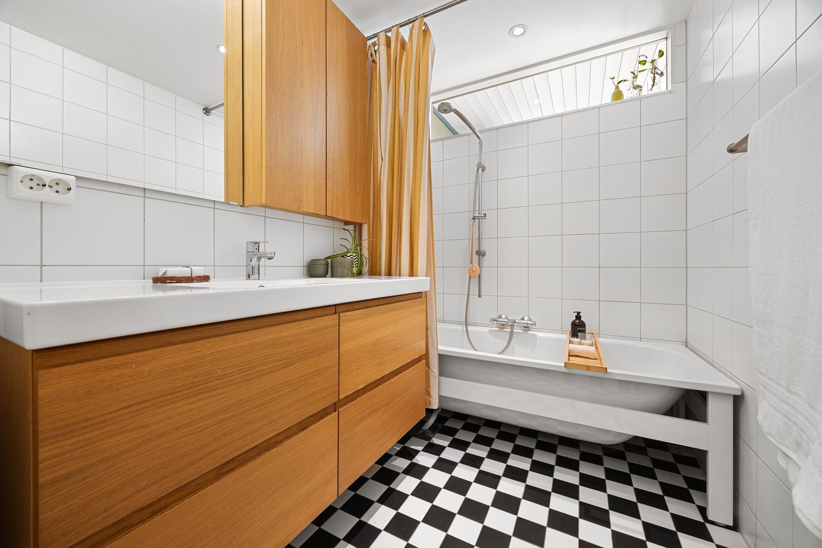 Pent, flislagt bad med gulvvarme. Badet inneholder badekar, heldekkende servant med skuffer under og speilskap over. Galleribilde