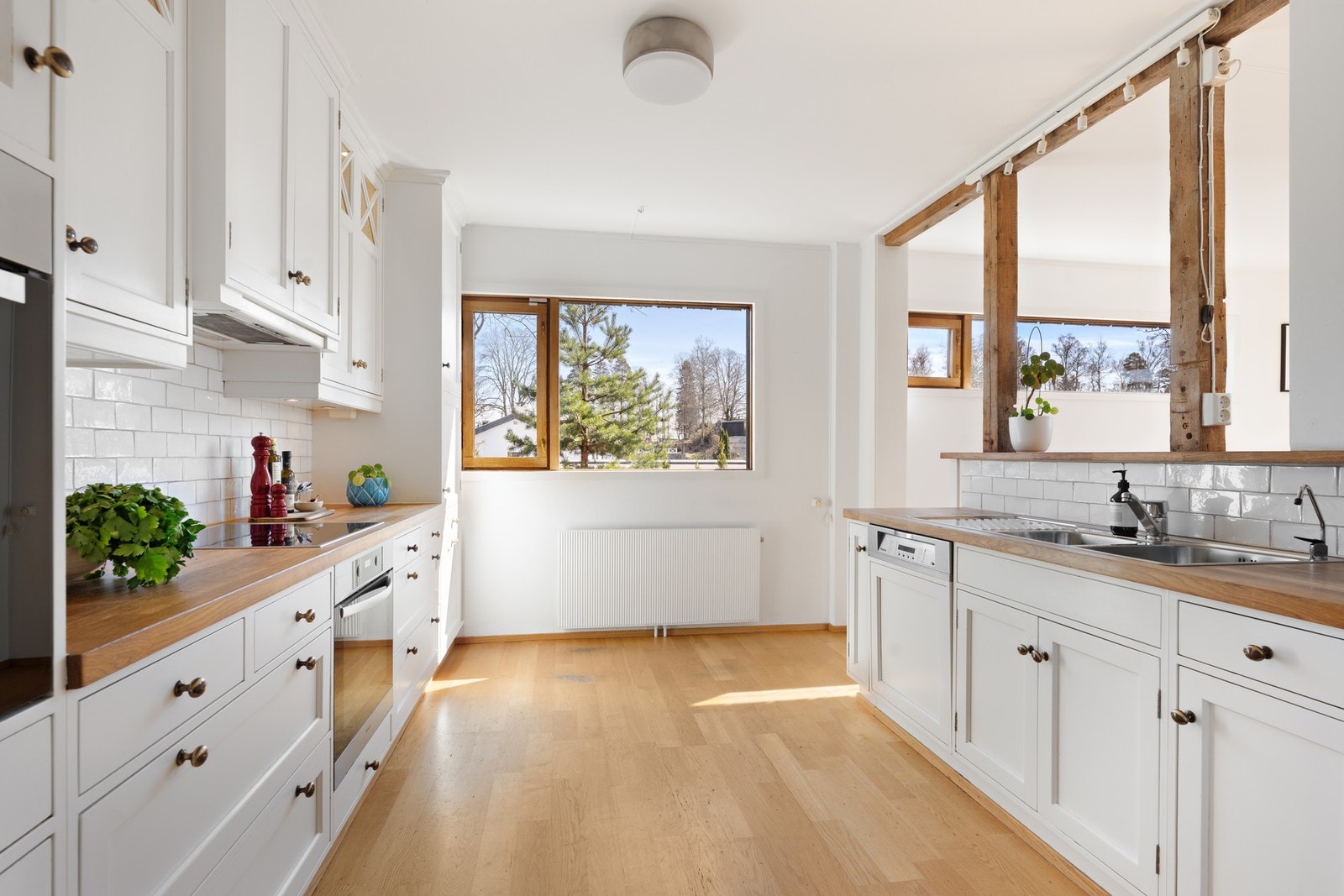 Heltre benkeplate med planlimt kum i rustfritt stål, ventilator og opplegg for både oppvaskmaskin og vaskemaskin. Kjøkkenet er fra Risør Snekkeri AS, med integrert induksjonstopp og stekeovn. Galleribilde