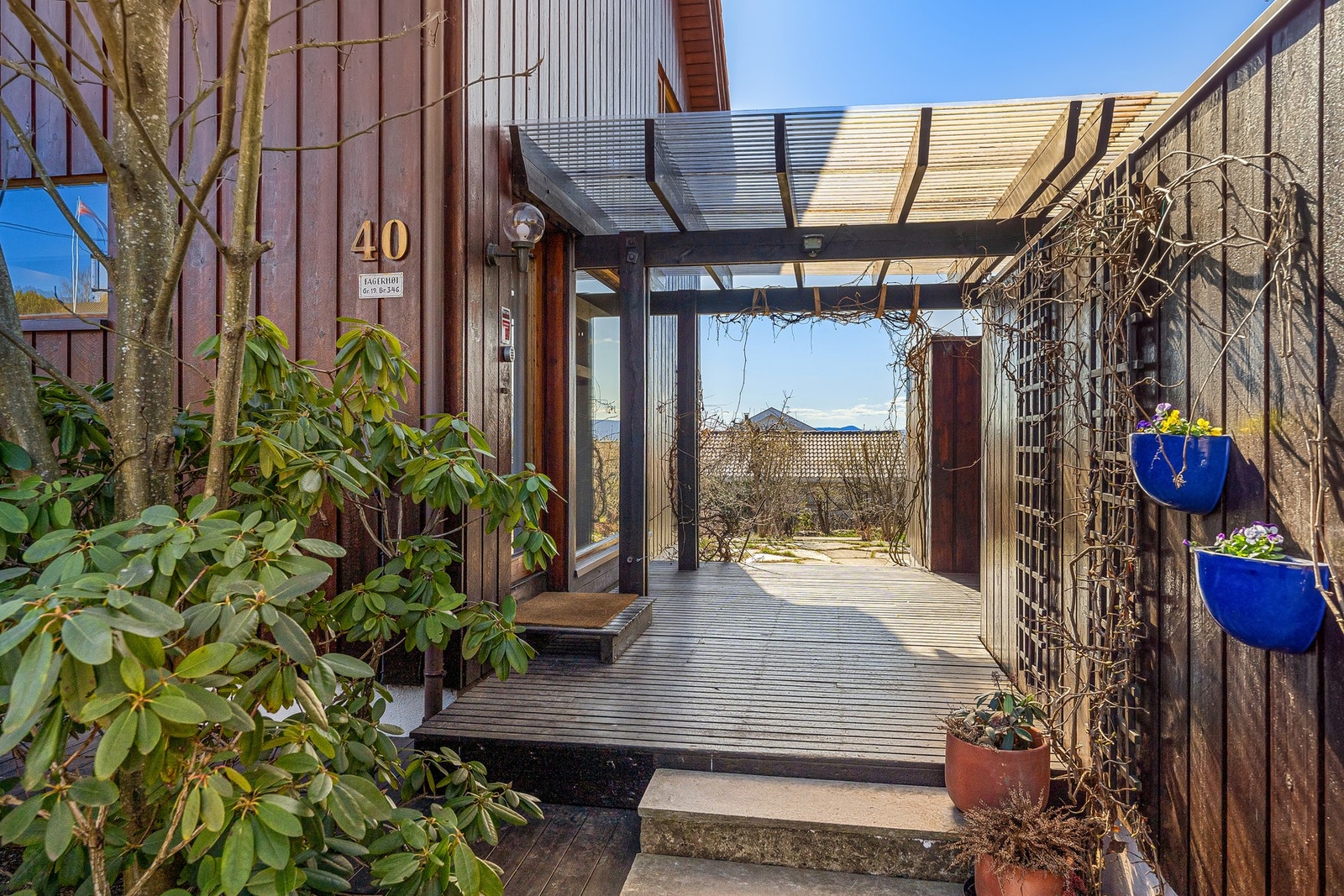 overbygget inngangsparti omkranset av frodig beplantning. Herfra har du både tilgang til garasje og en romslig utebod. Galleribilde