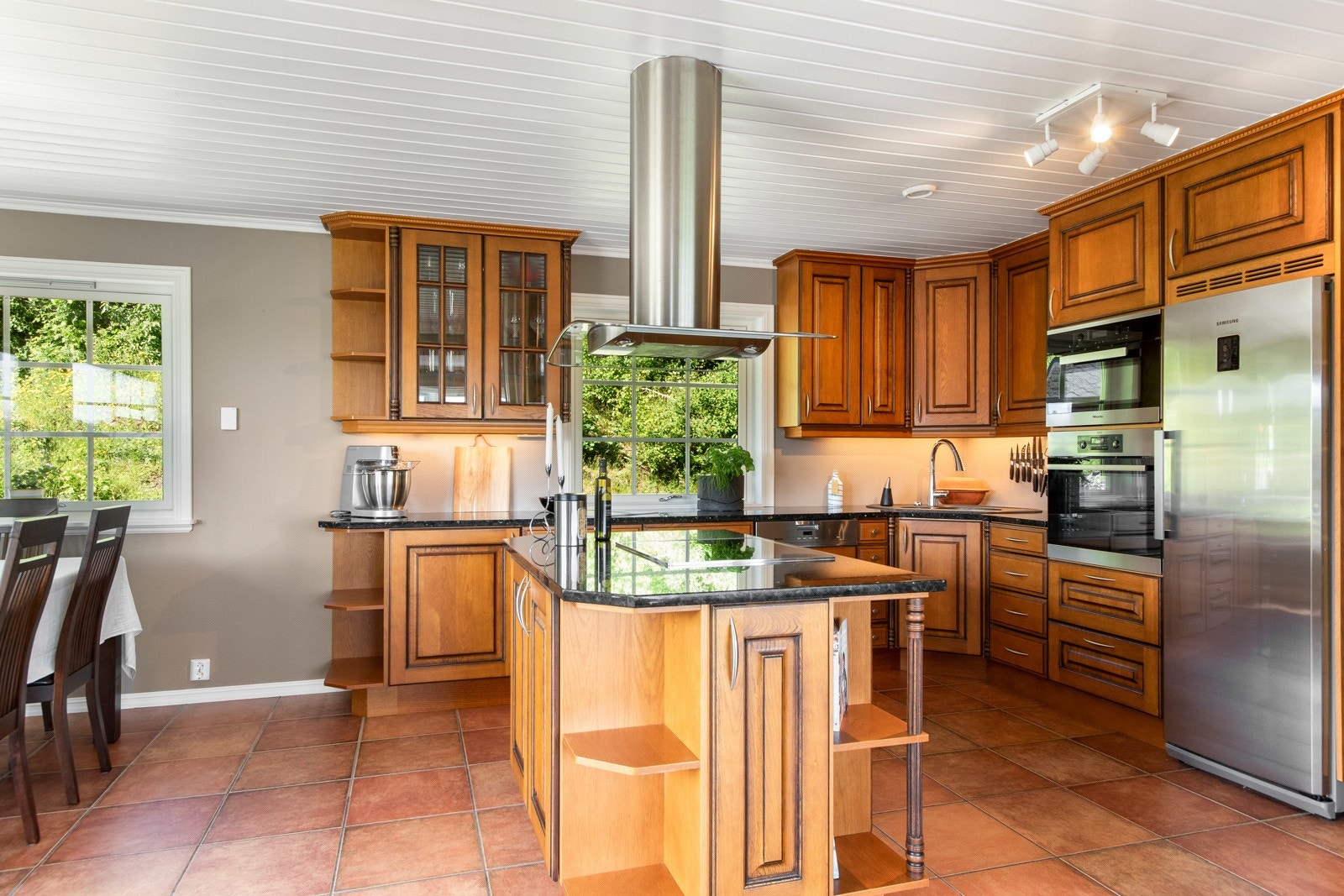 Den sentrale kjøkkenøya med integrert kokeplate og avtrekksvifte gir en praktisk arbeidsplass, samtidig som den innbyr til sosial matlaging. Galleribilde