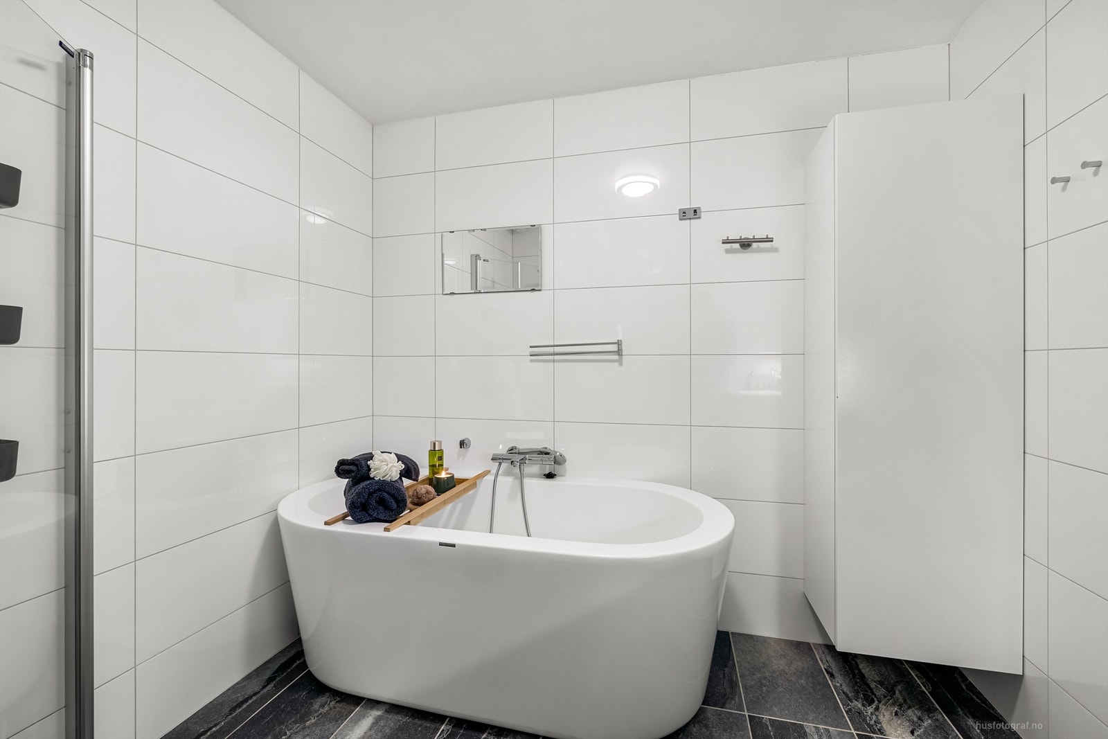 Badet har frittstående badekar med veggmontert hånddusj og dusjhjørne med foldedører av glass Galleribilde