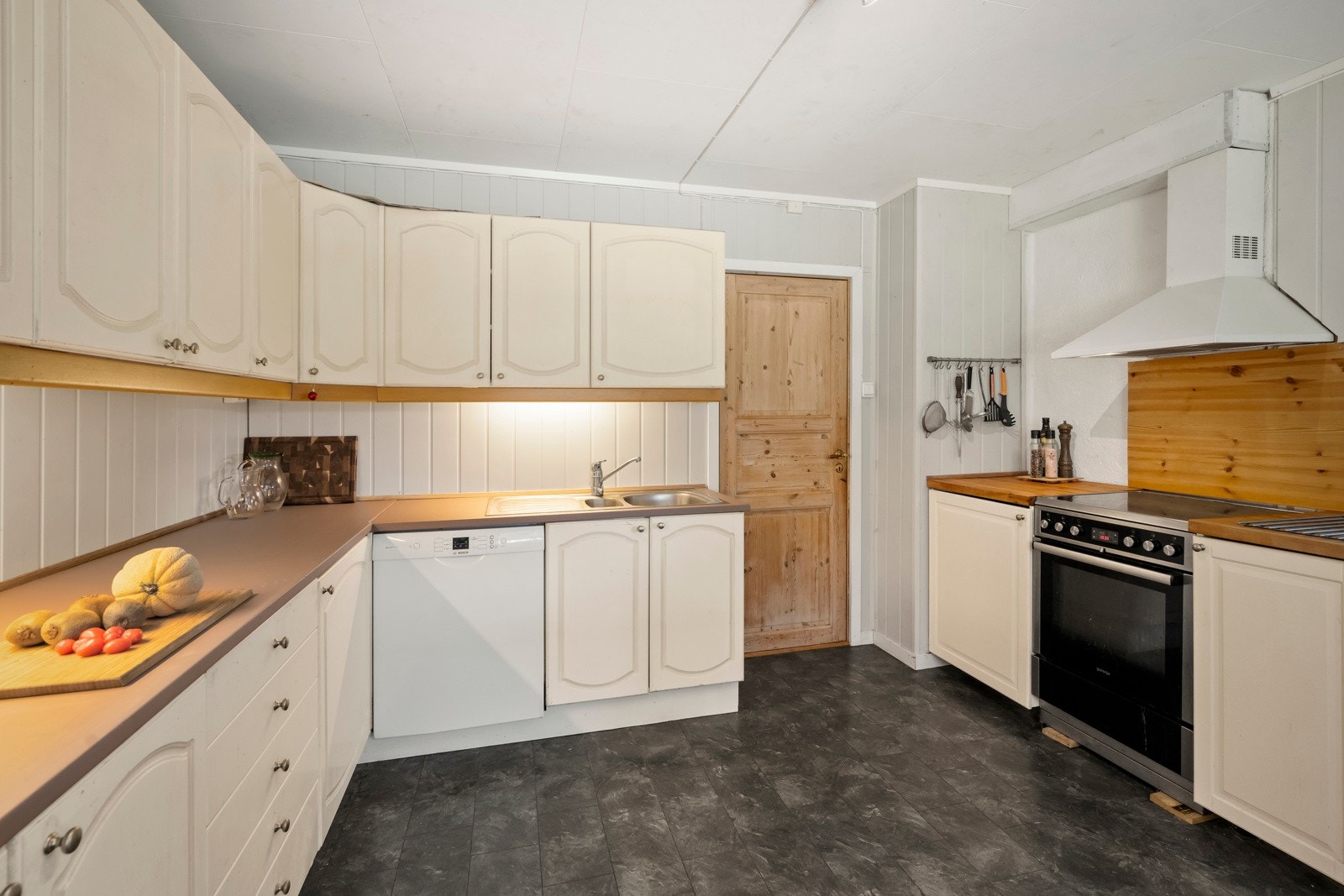 Kjøkkenet har innredning med profilerte fronter. Benkeplaten er av heltre. Det er kjøleskap, oppvaskmaskin og komfyr. Galleribilde