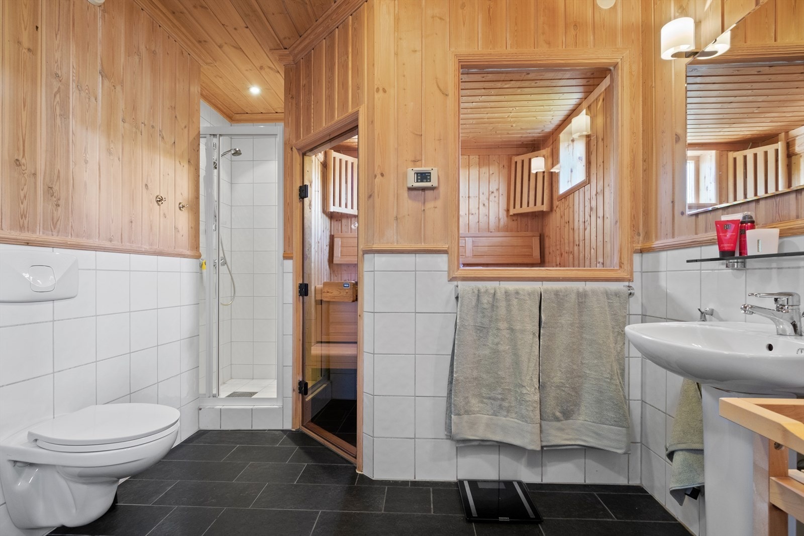 Gjestebadet i 1. etasje har fliser på gulv med vannbåren gulvvarme og fliser og panel på vegger. Badet er utstyrt med søyleservant, dusjnisje og WC. Det er adkomst til badstue. Galleribilde