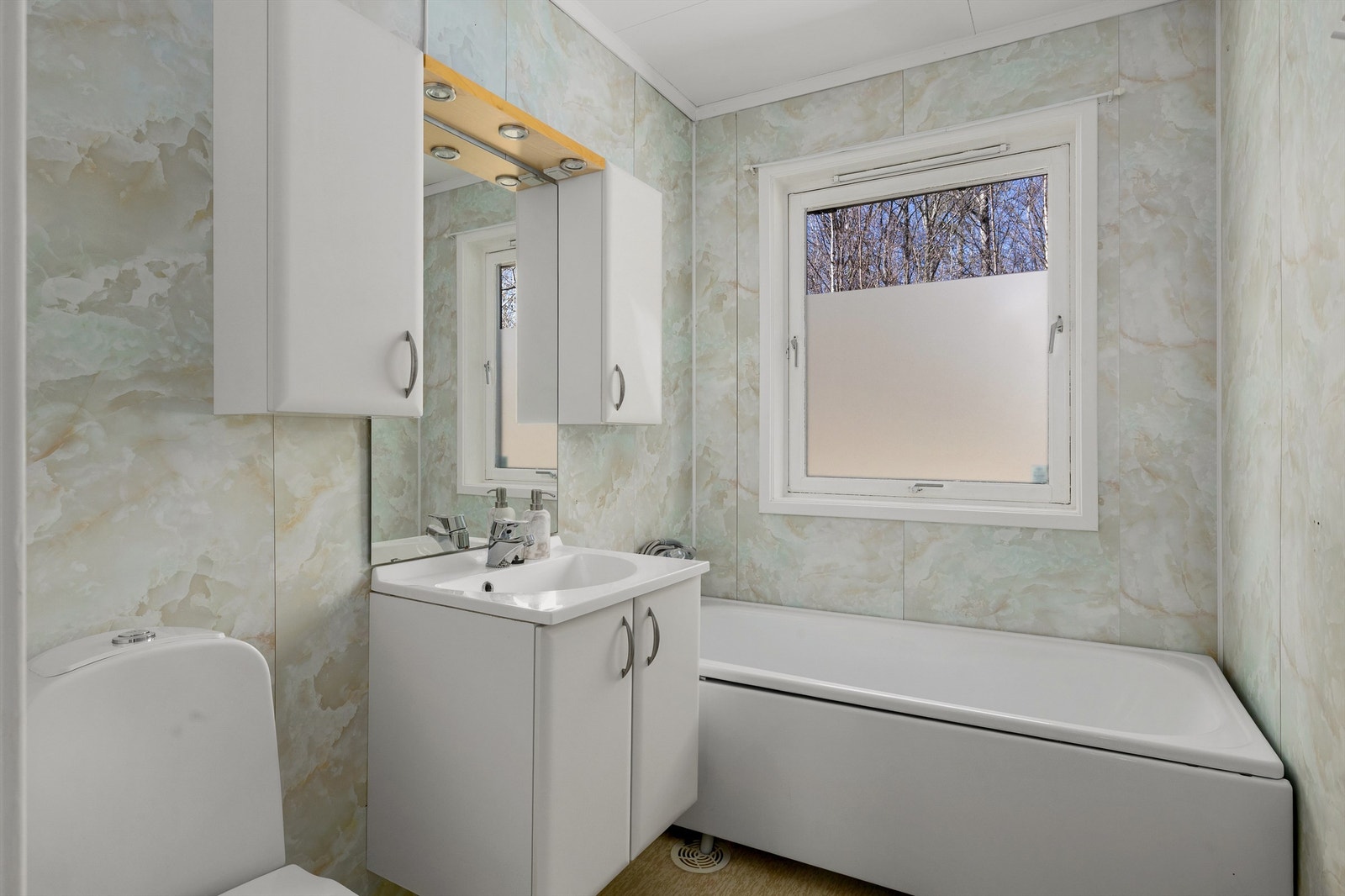 Badet har servant i innredning, badekar og gulvsatt toalett Galleribilde
