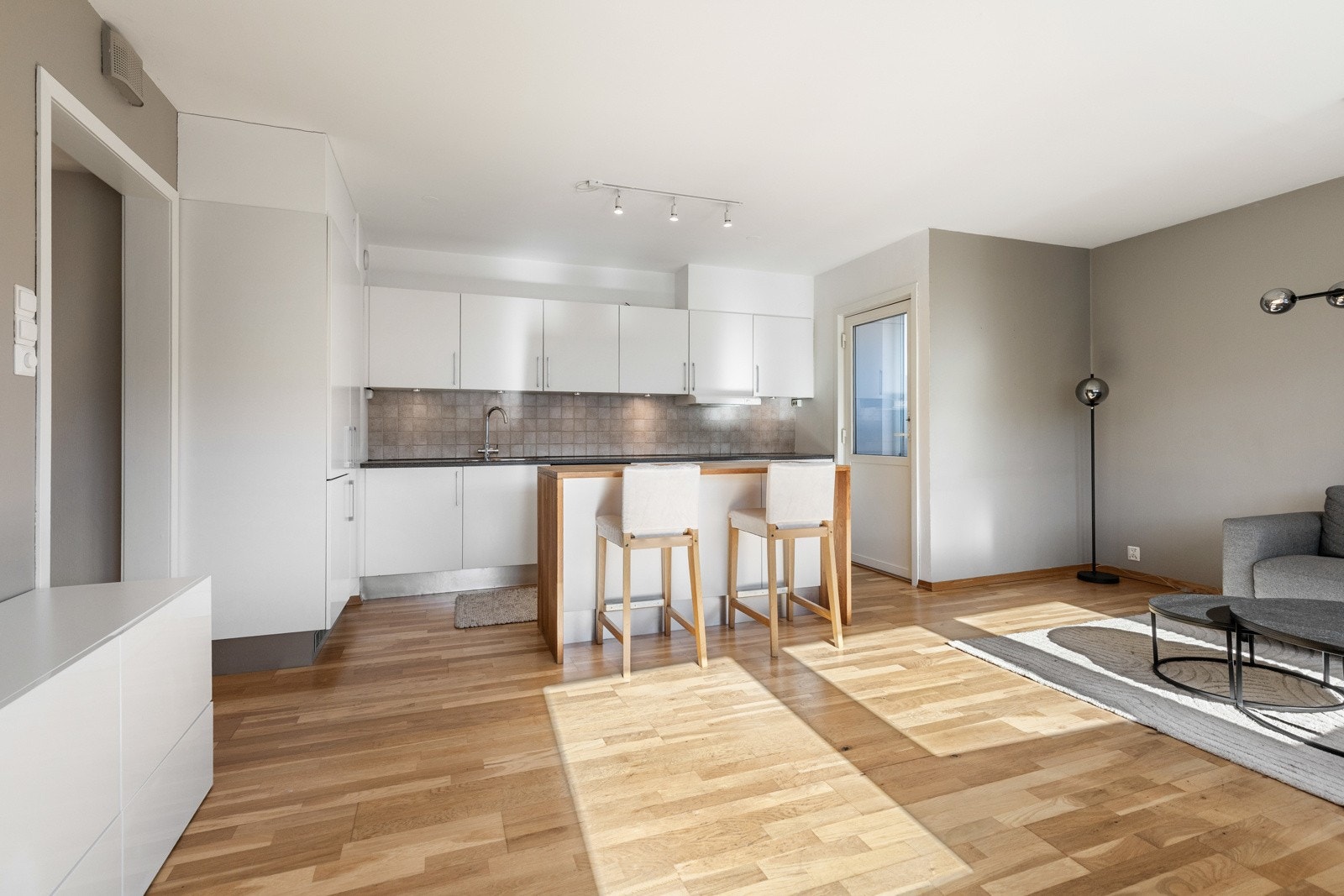 En glassdør fører ut til balkongen, og parkett på gulvet kombineres med vegger malt i hvitt og en dus gråtone. Galleribilde