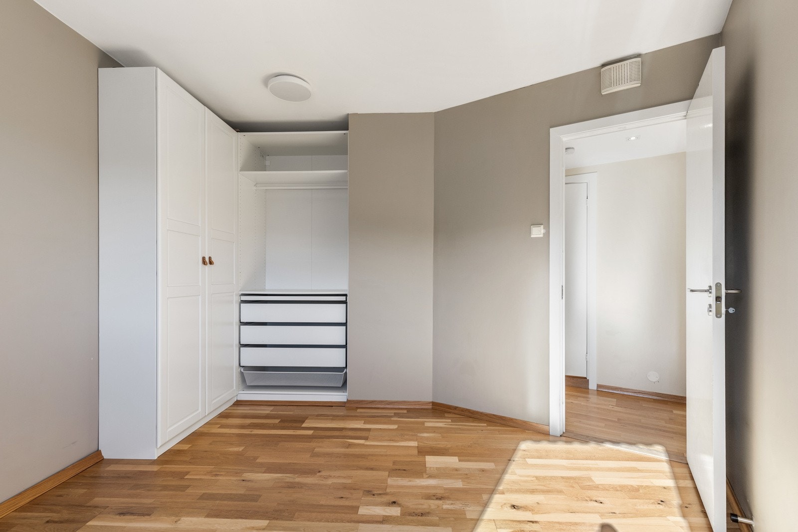 Soverommet har en smart garderobeløsning med hvite skap montert på hver sin side av den avsatte plassen for seng. Galleribilde