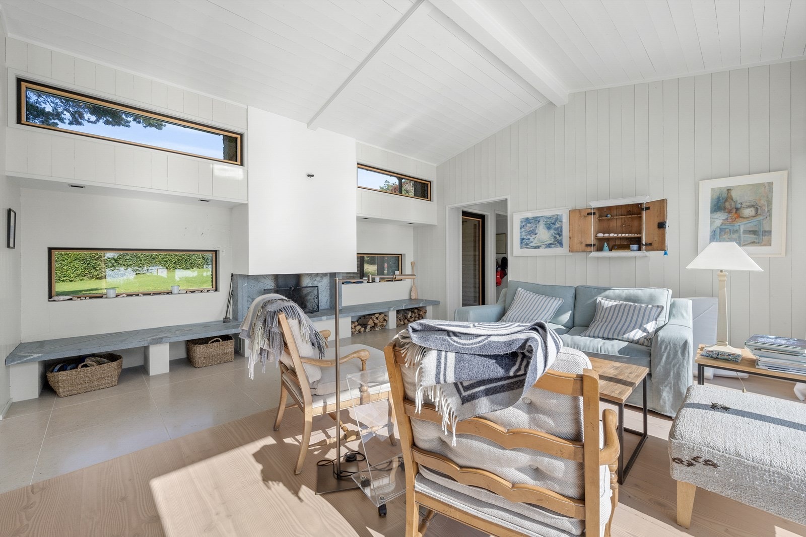 Langveggen mot nord har en åpen peis og smale vinduer i to høyder som gir glimt av himmel og bakhage. Galleribilde