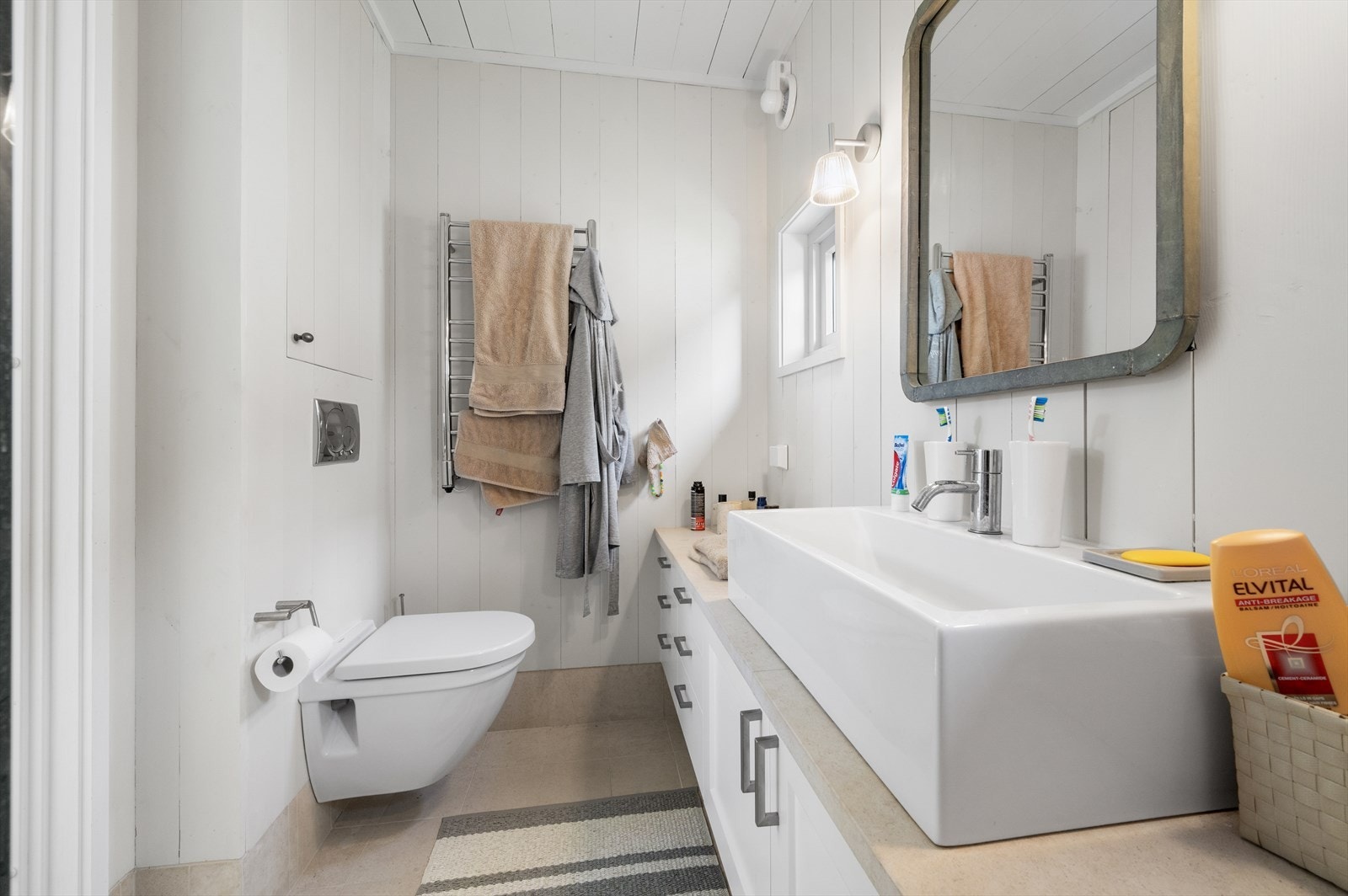 Masterbadet er pent innredet med veggmontert toalett, langstrakt servantinnredning og regnfallsdusj. Galleribilde