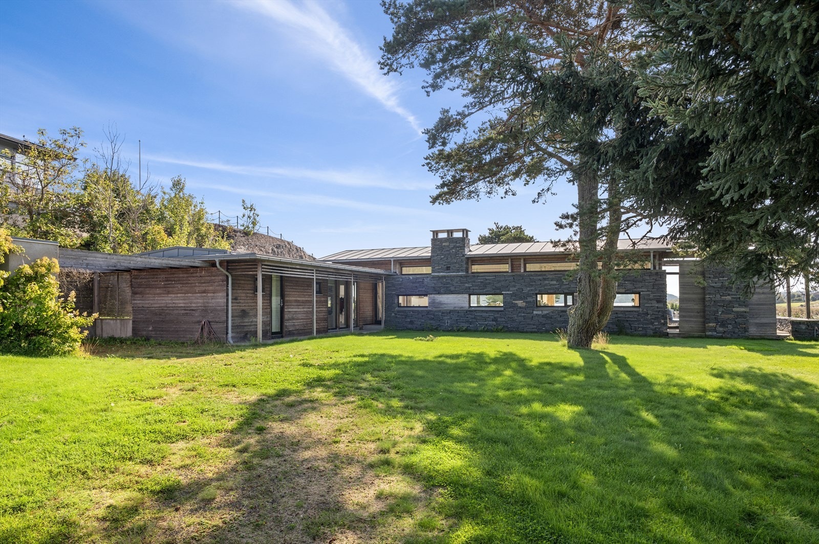 Hytta er kledd i ubehandlet, naturlig grånet tre, kombinert med lokal skifer/tørrmur og tak tekket i sink. Galleribilde