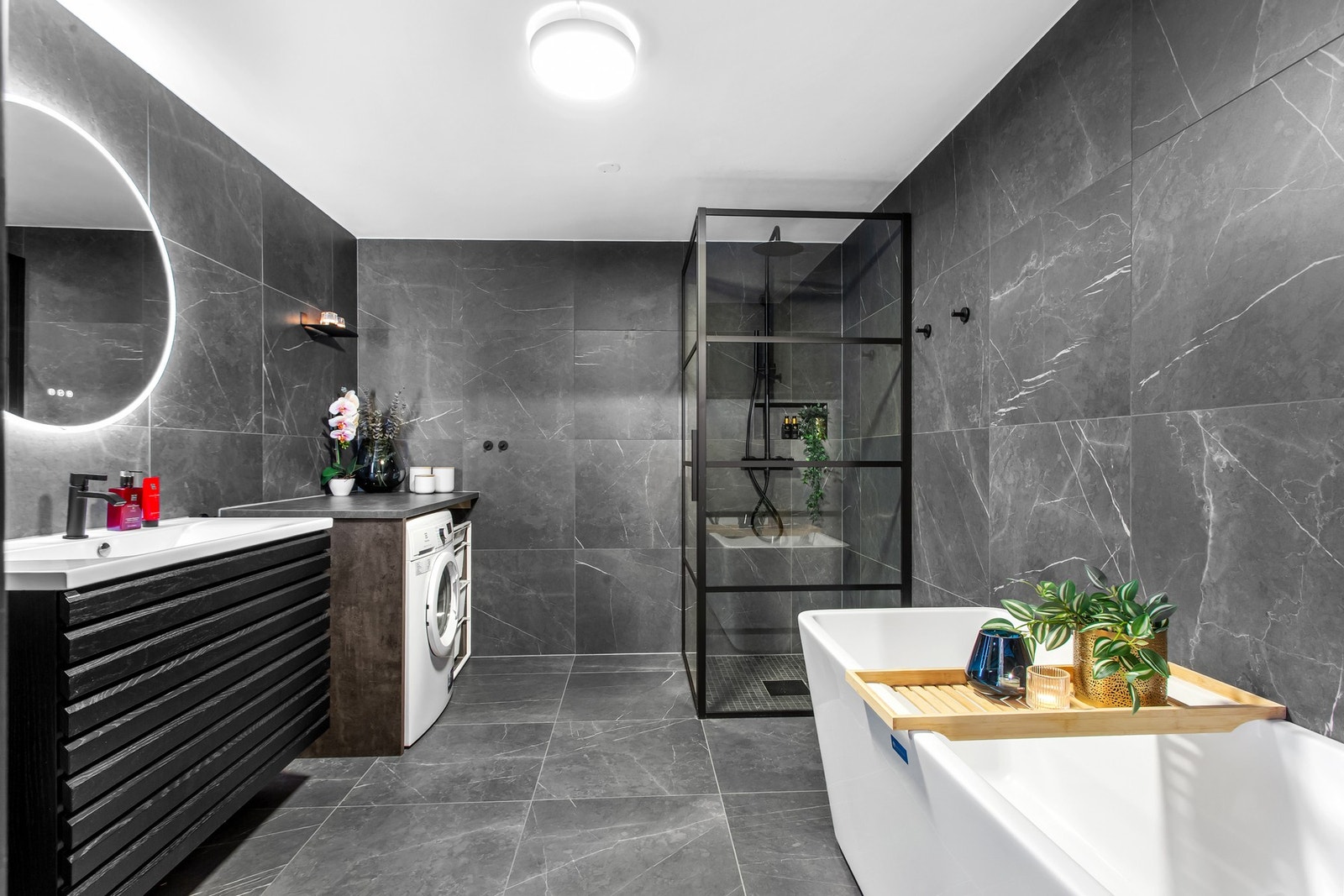 Boligens store hovedbad oser av luksus med gulvvarme, badekar, dusjhjørne med regnfallsdusj samt opplegg for vaskemaskin og tørketrommel Galleribilde