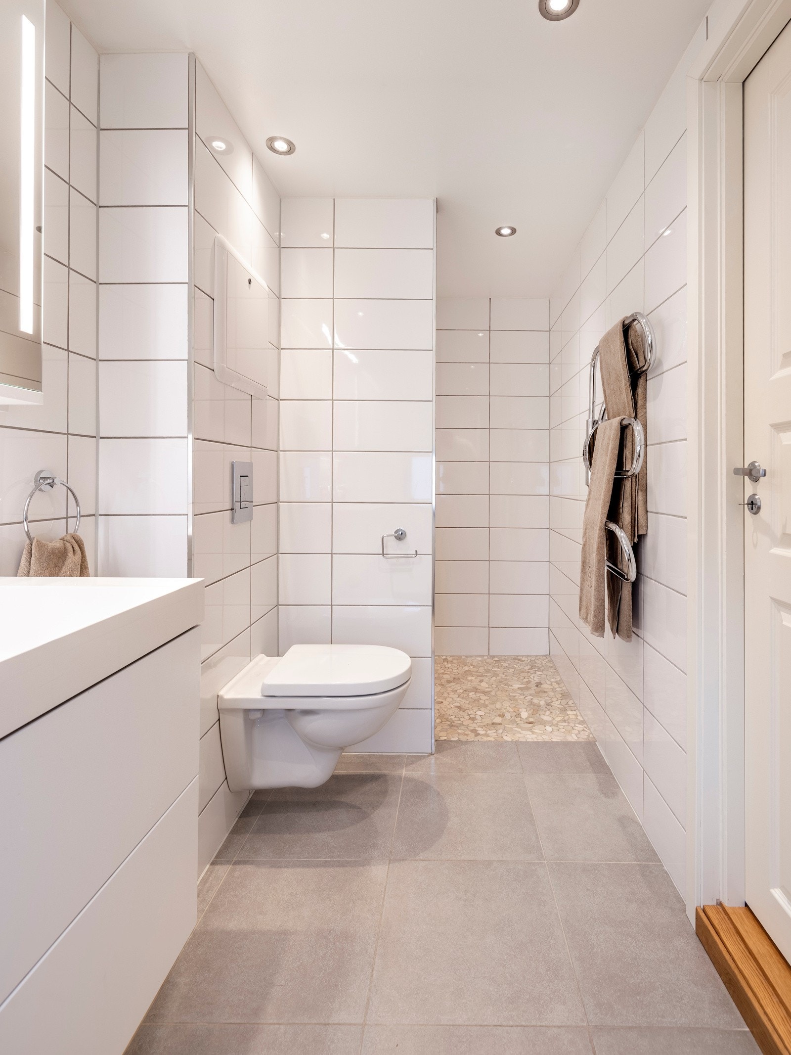 Baderomsinnredningen består av en heldekkende dobbelservant på hvit skuffeseksjon, matchende høyskap, et bredt speilskap med integrert belysning og et veggmontert toalett. Galleribilde