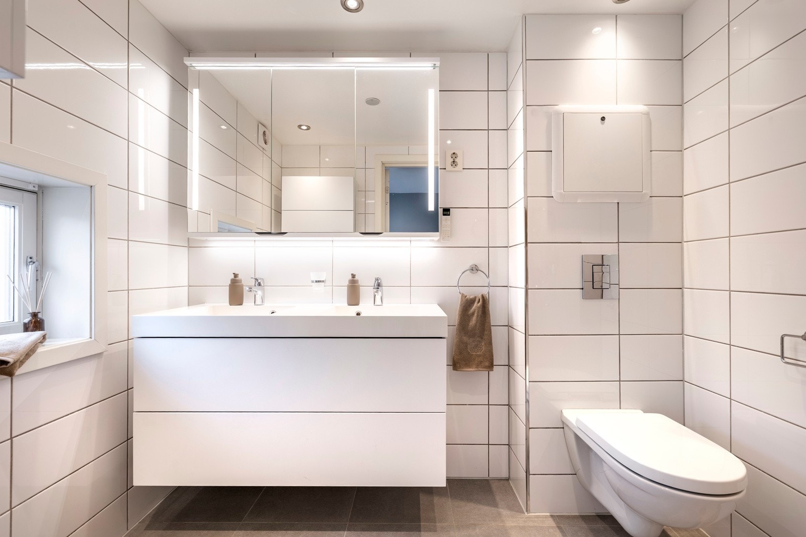 Badet ble pent pusset opp i 2015 og fremstår moderne. Badet er utført med grå fliser på gulvet, hvite fliser på veggene og gulvvarme. Det er dimmbare LED downlights i himlingen og dagslys fra et smalt vindu. Galleribilde