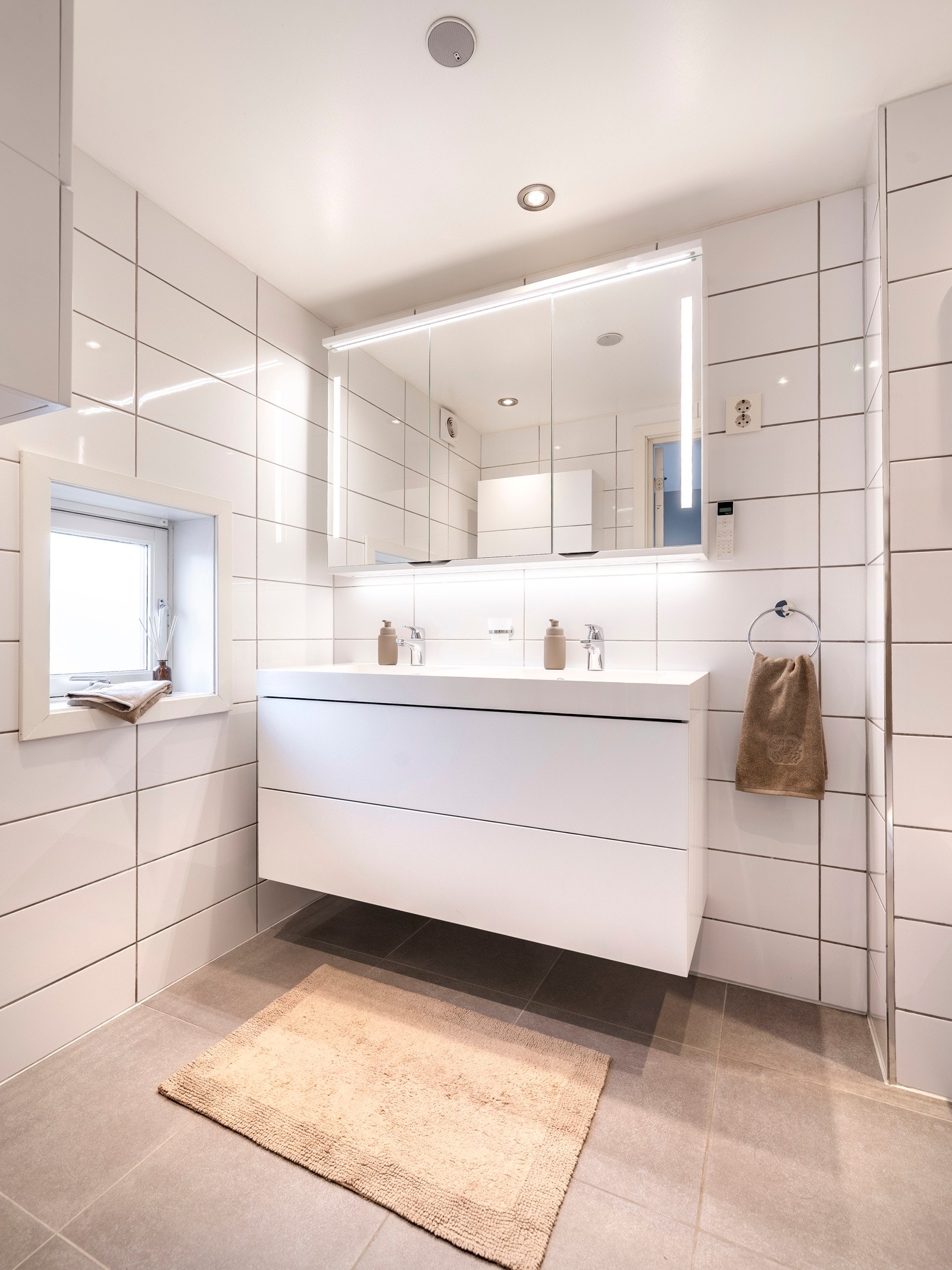 Badet ble pent pusset opp i 2015 og fremstår moderne. Badet er utført med grå fliser på gulvet, hvite fliser på veggene og gulvvarme. Det er dimmbare LED downlights i himlingen og dagslys fra et smalt vindu. Galleribilde