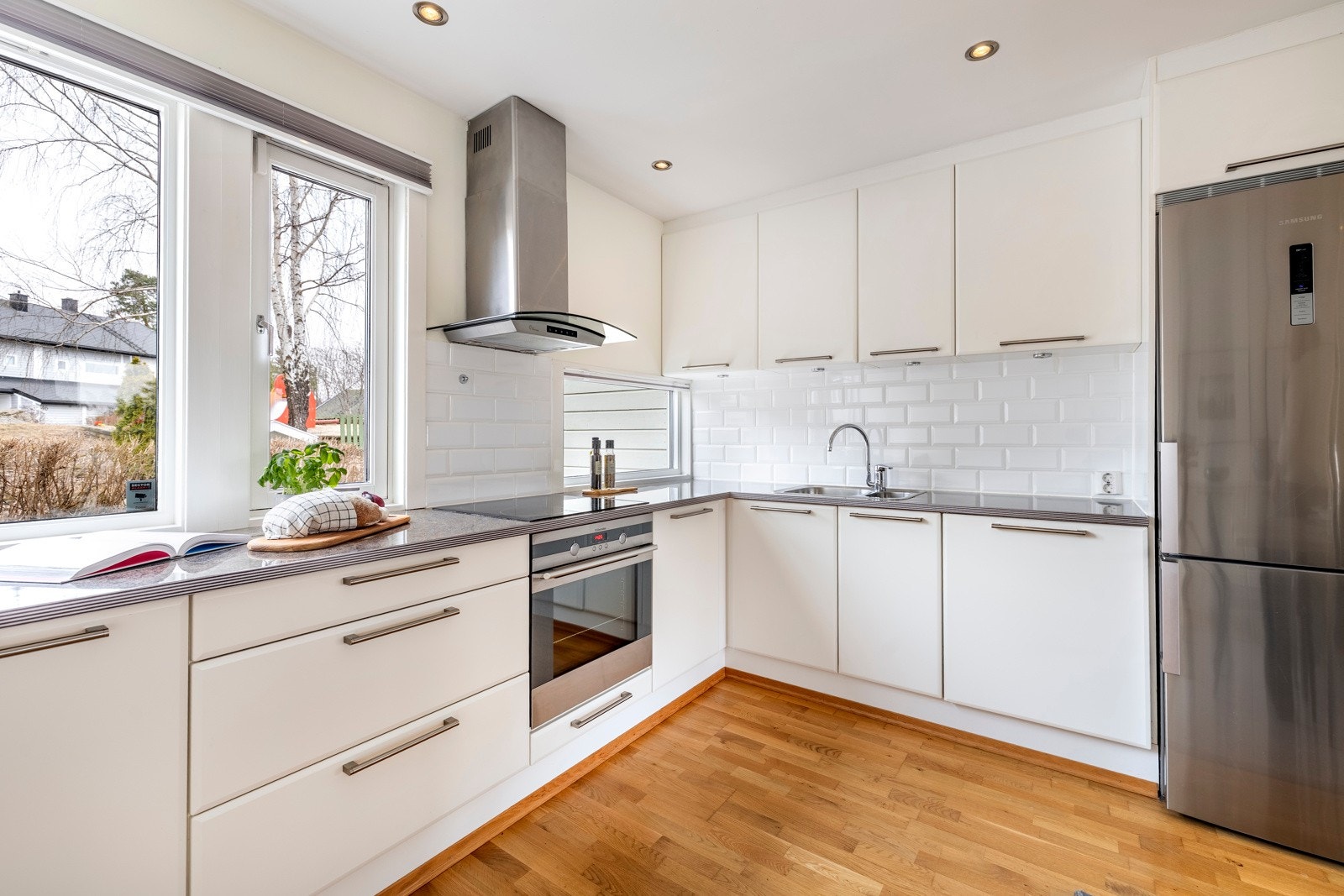 Kjøkkenet har integrert stekeovn, platetopp, oppvaskmaskin og nisje til kjøleskap. En ventilator i stål er montert over kokesonen og det er lagt hvite metrofliser over benken. Over i rommets spisesone er det montert flere vegghengte skap. Galleribilde