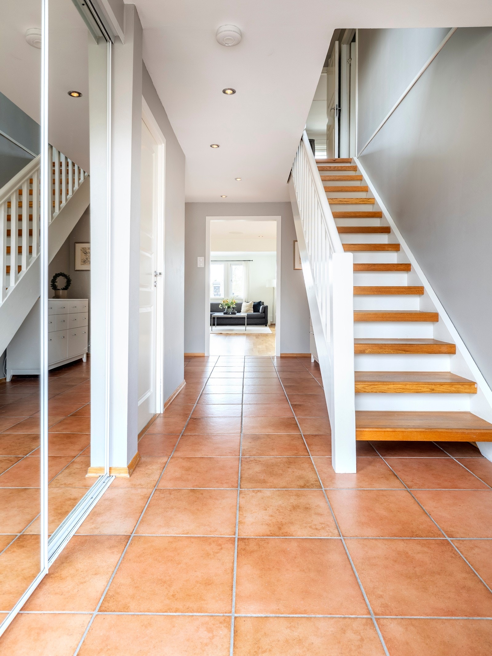 Entreen har terrakottafargede fliser på gulvet med varmekabler og en hvitmalt trapp med eiketrinn som fører opp til andre etasje. I den ene veggen er det innfelt en skyvedørsgarderobe med speilfronter. Galleribilde