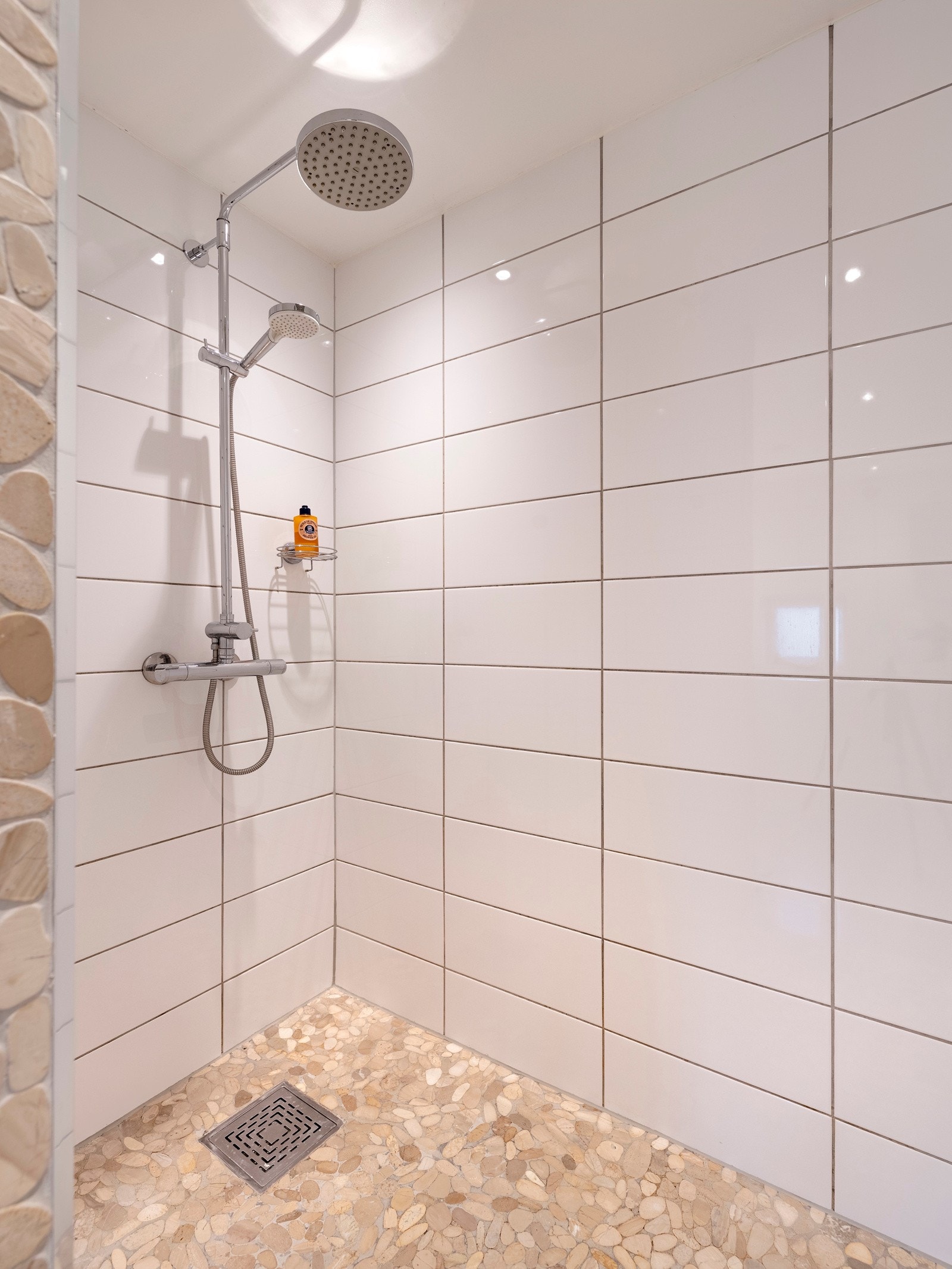 Dusjnisjen har beige elvesteiner på gulvet, regnfallsdusj og hånddusj. Galleribilde