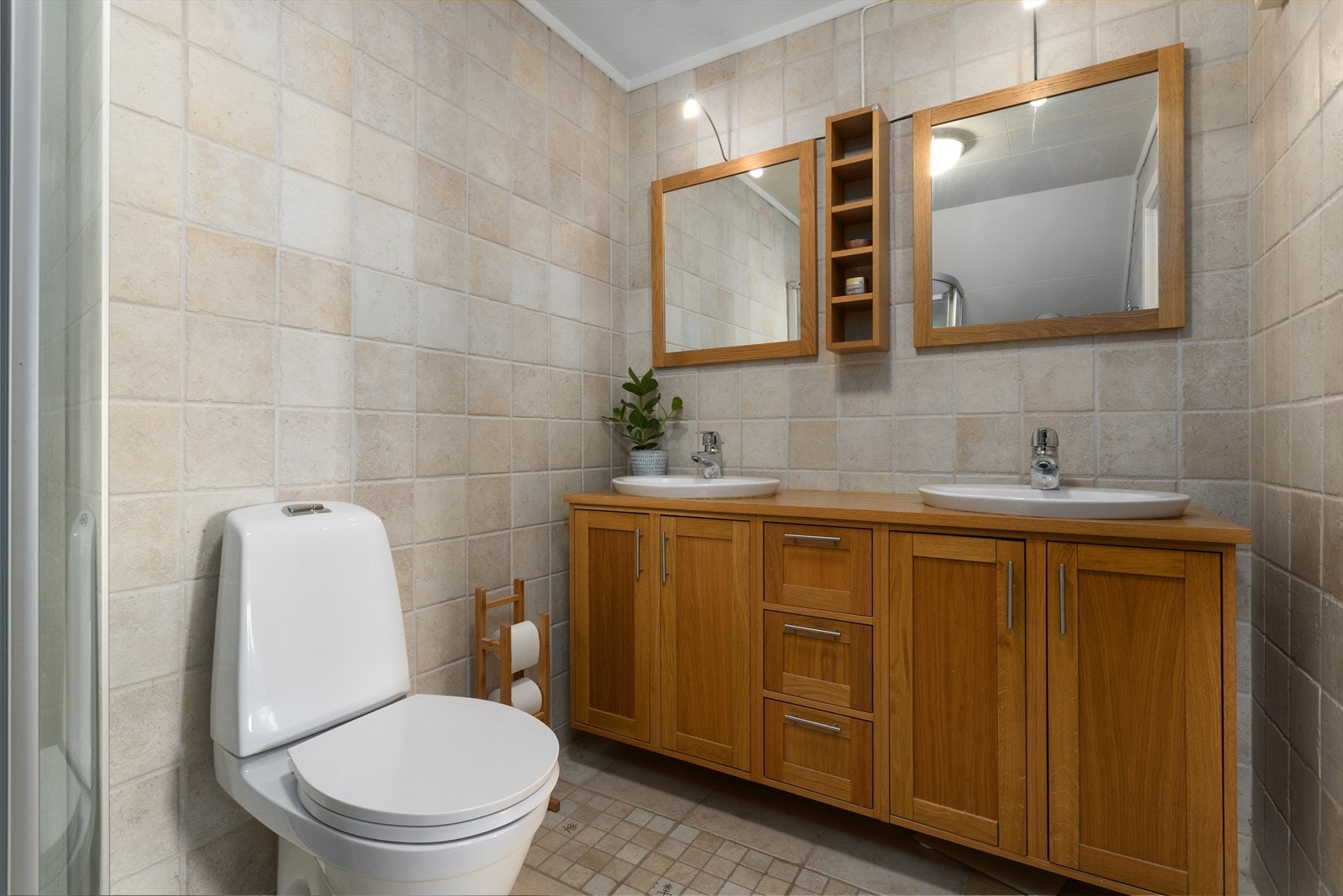 Badet er fra 2005 og har flislagte overflater på gulv og vegger. Videre er det en romslig servantinnredning med dobbel servant, toalett og speil med lys over. Galleribilde