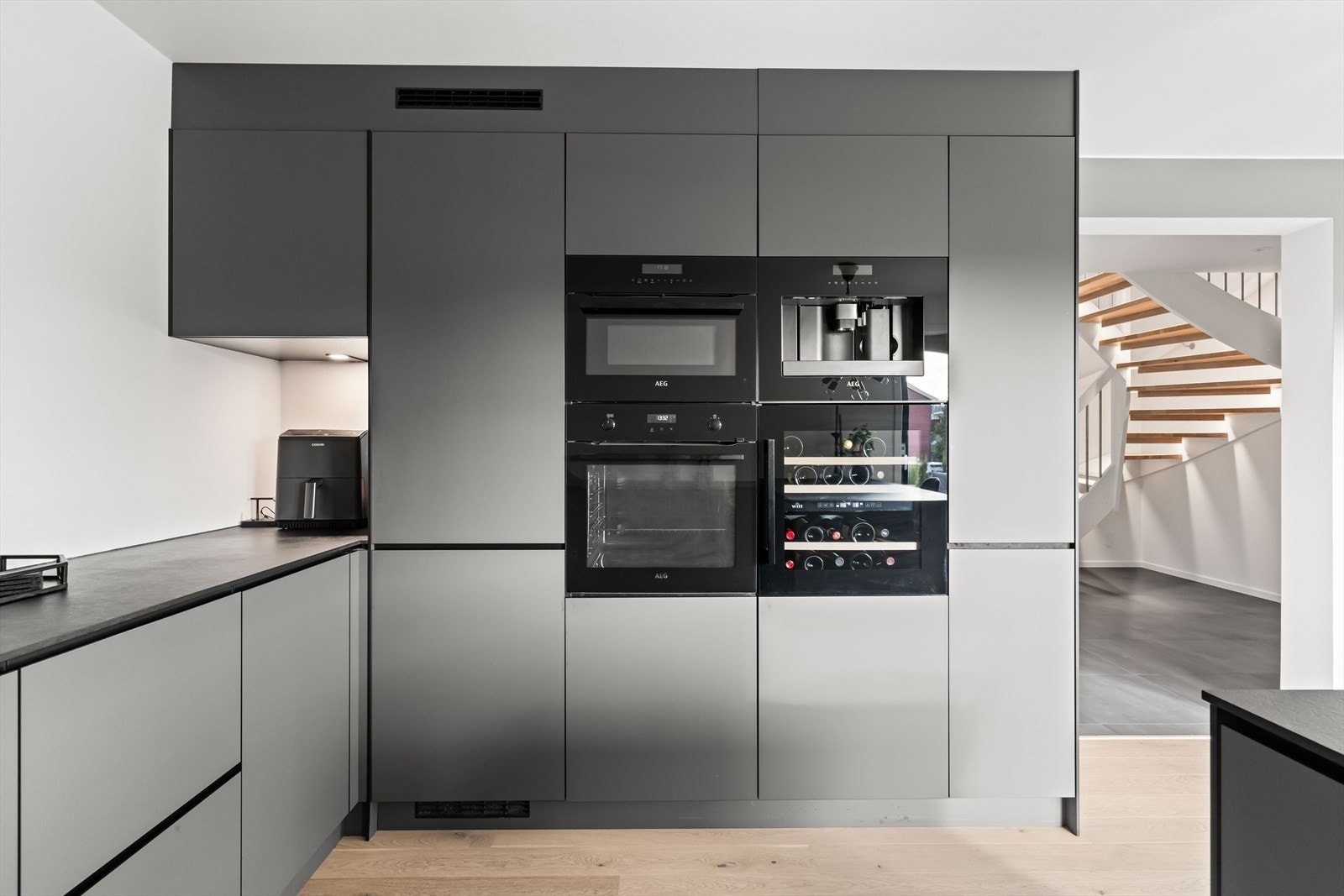 Innredningen er i mørk grå utførelse med slette fronter, og benkeplate med navn "Blackstone med sort kjerne". Hvitevarene er integrerte, bestående av komfyr, kombiovn, vinskap, kaffemaskin, oppvaskmaskin og kjøleskap. Galleribilde
