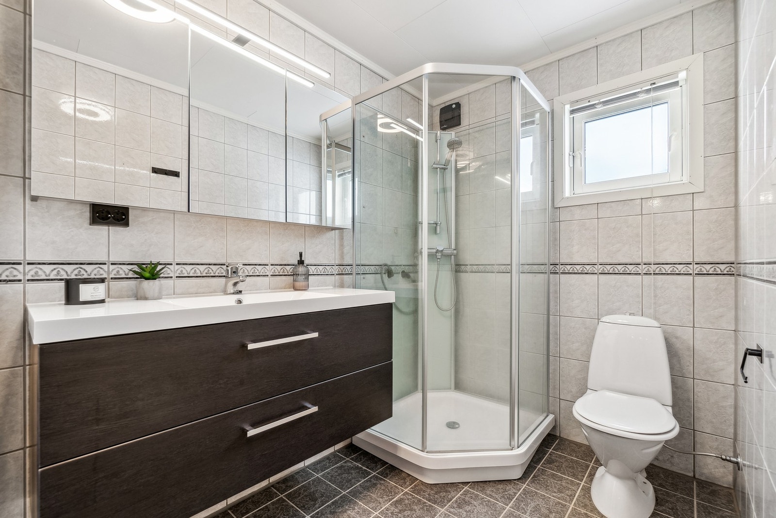 Badet er fra byggeår, men fremstår tidløst takket være en lys utførelse på vegger mot en mørk utførelse på gulv og deler av innredningen. Galleribilde