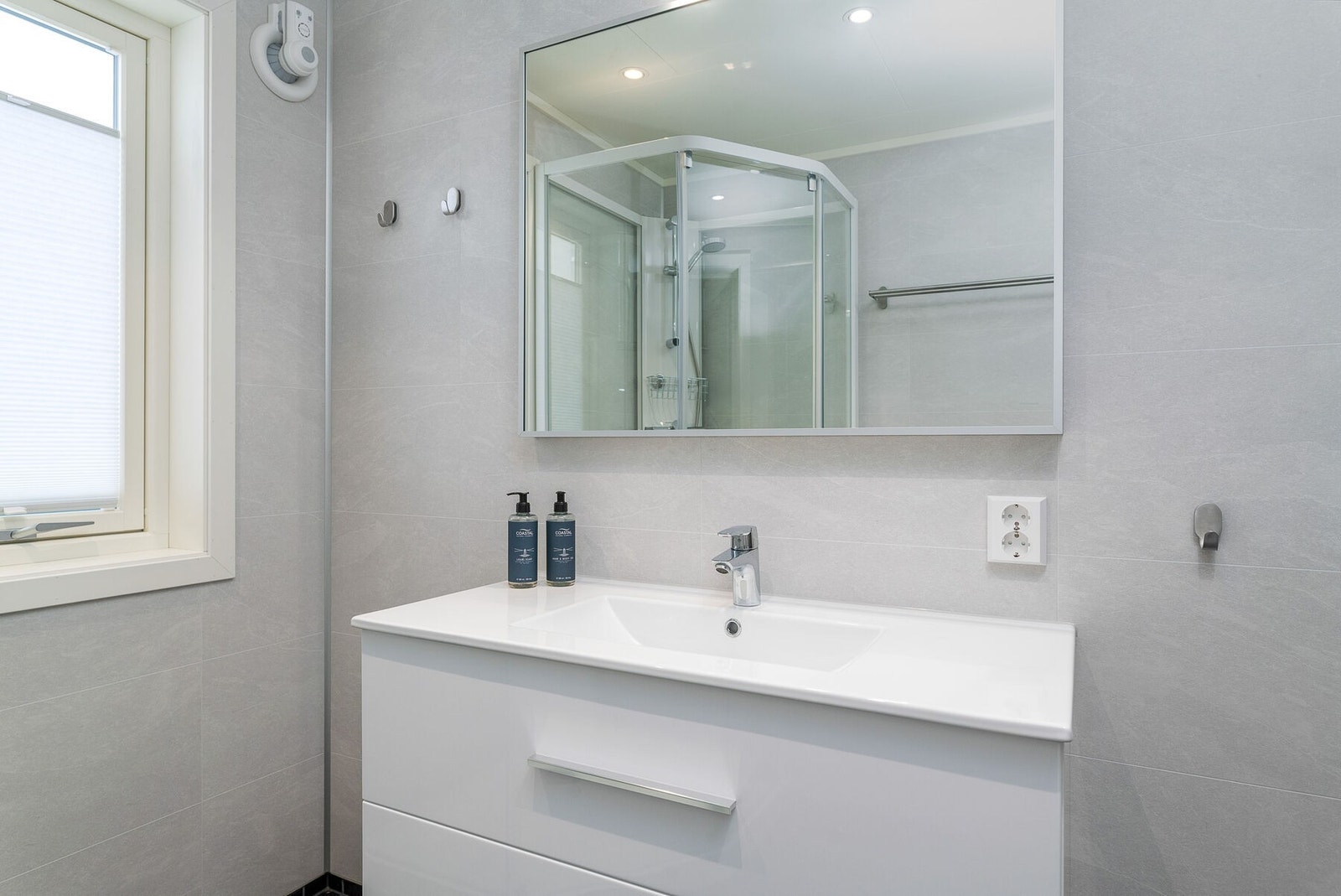 Lys og moderne innredning med skuffer, servant og speil. I tillegg er det dusjkabinett og wc. Galleribilde