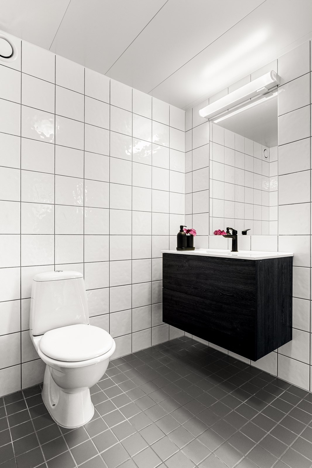 Pent og delikat baderom. Stilfulle glatte fronter, heldekkende servant med porselenstopp. Speil og lysarmatur på vegg over servanten. Galleribilde