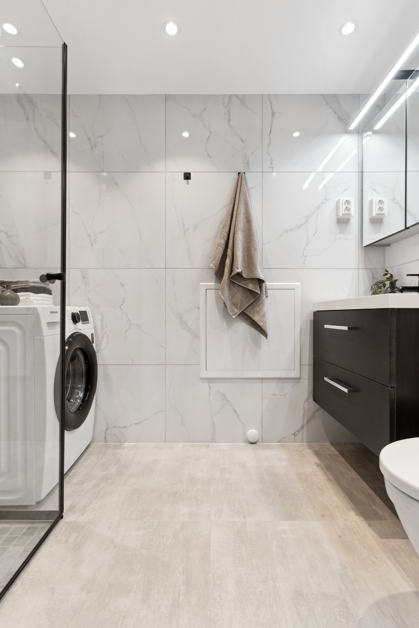 Delikat baderom med store, marmorerte fliser, integrert belysning og praktisk oppbevaring. Her er alt nytt og ubrukt. Galleribilde