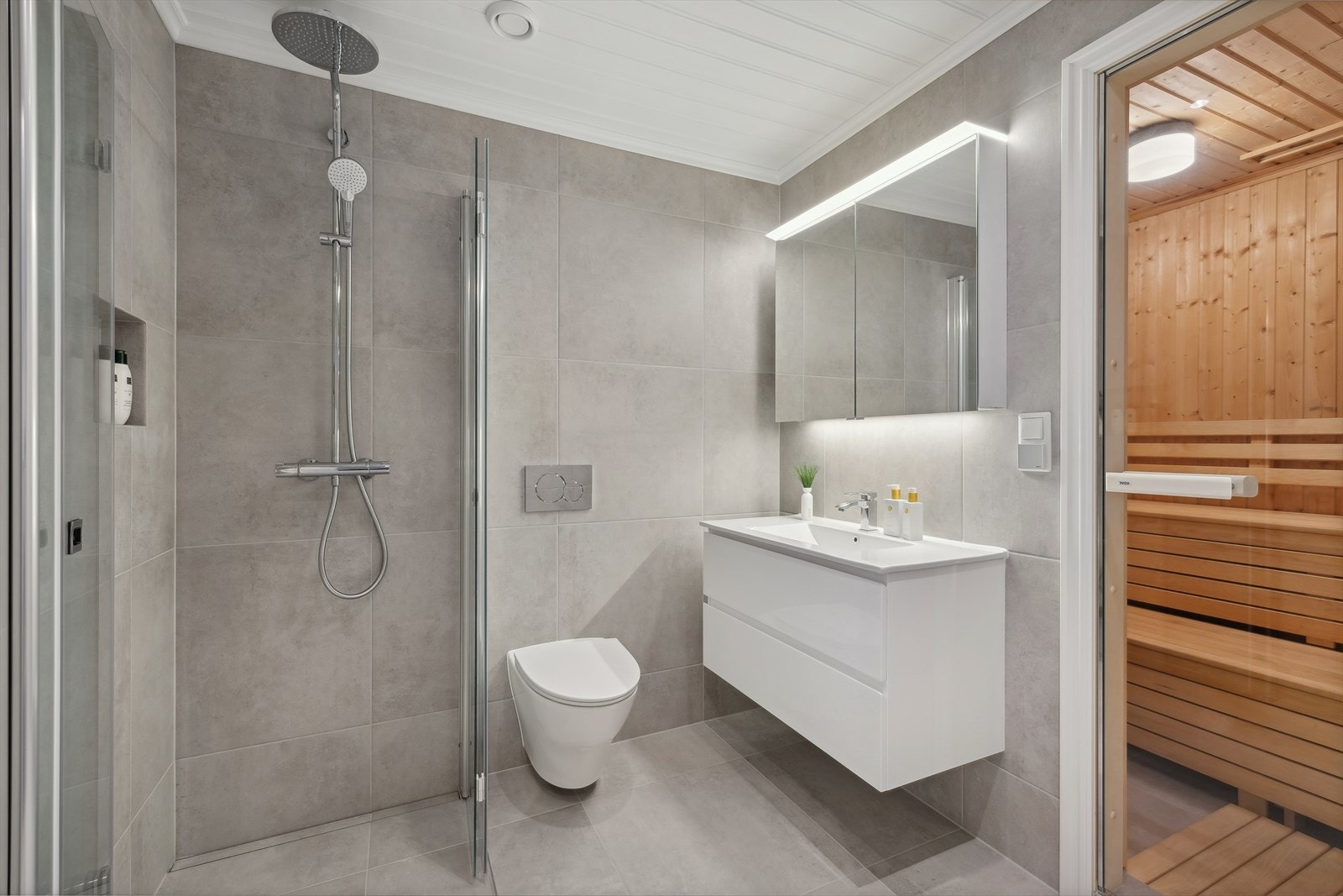 Lyst flislagt bad med dusjhjørne, vegghengt wc og flott baderomsinnredning. Varmekabler i gulv Galleribilde