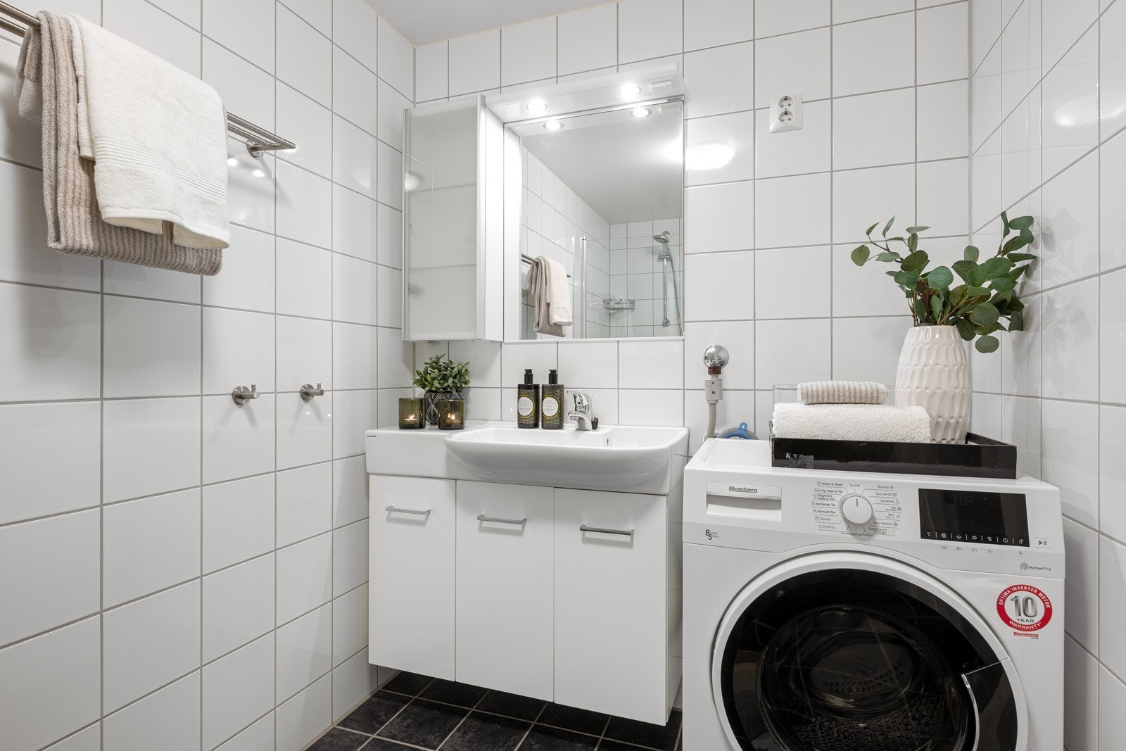 Moderne helfliset baderom med varmekabler i gulv. Badet inneholder: servant med møblement, speil og belysning, vegghengt wc, dusj og opplegg for vaskemaskin. Plass til tørketrommel Galleribilde