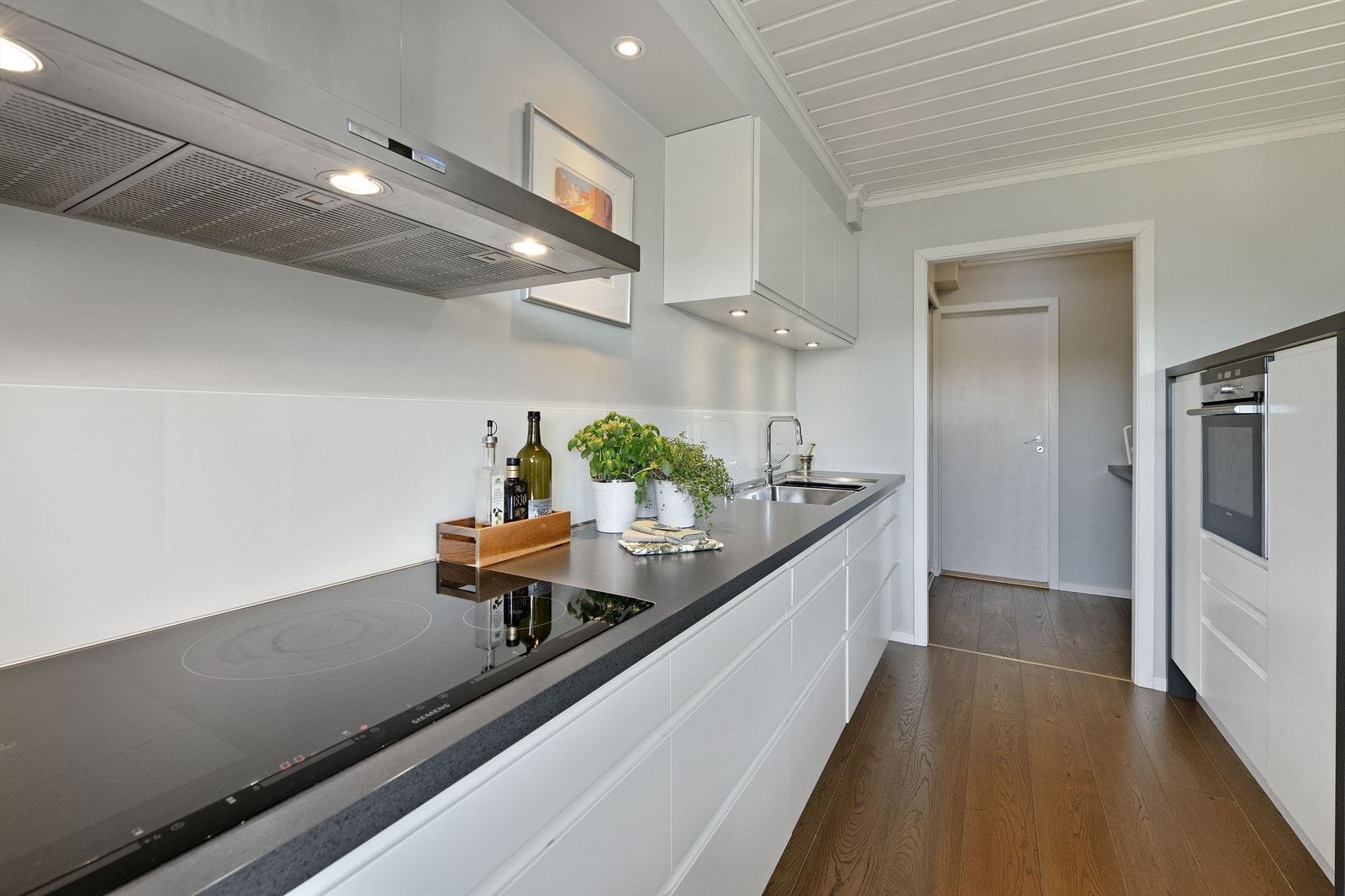 Kjøkken - integrerte hvitevarer følger; bred induksjon platetopp, oppvaskmaskin og komfyr - videre inngang til grovkjøkken (med bl.a. kjøleskap) og videre adkomst til bod Galleribilde