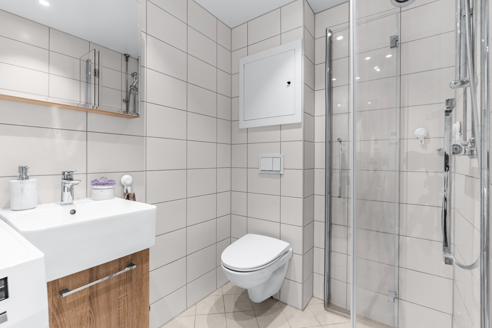 Videre er det et veggmontert toalett, dusjhjørne med to foldedører i glass, samt opplegg for vaskemaskin. Galleribilde