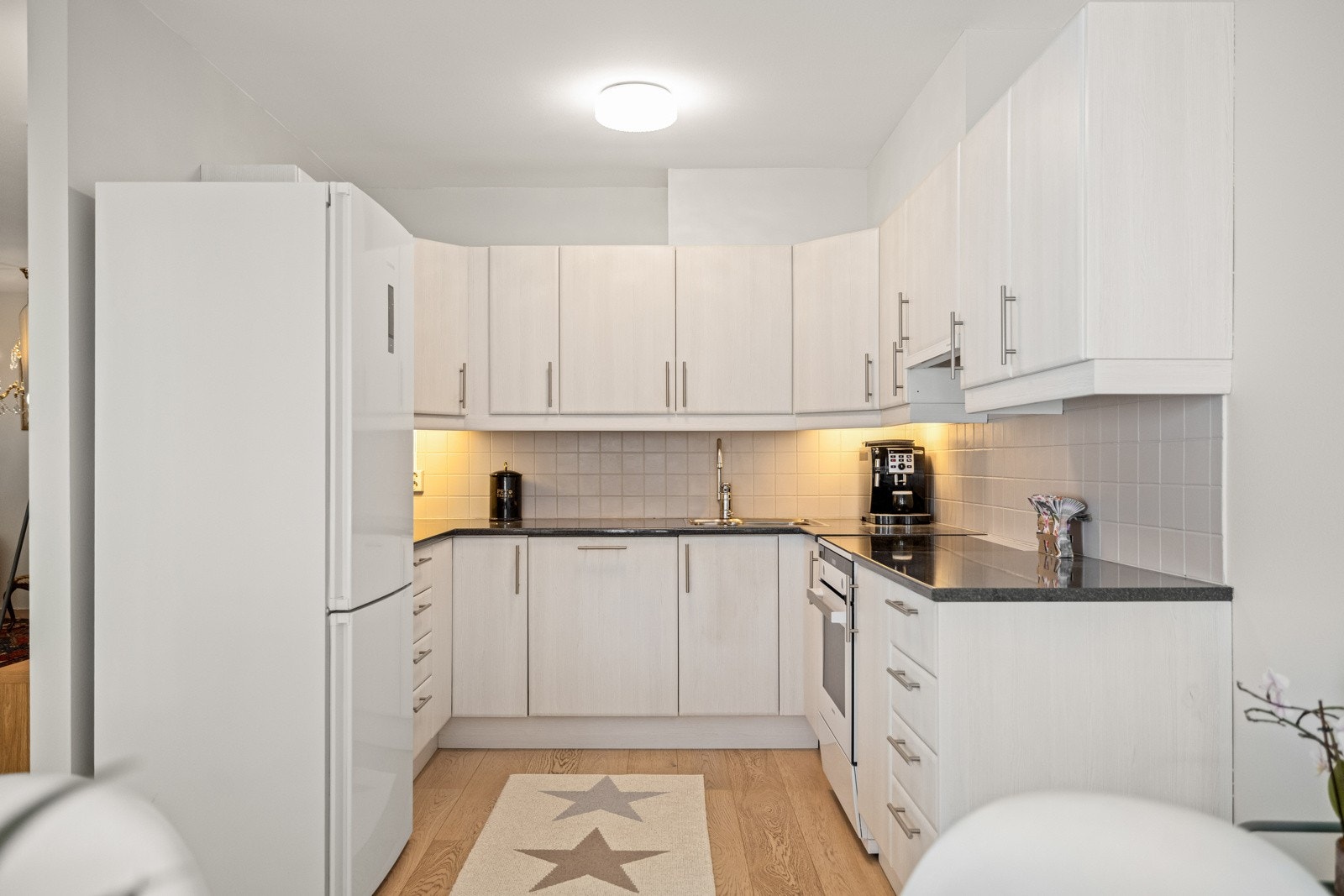 Kjøkkenet har slett innredning, laminat benkeplate og fliser mellom benk og overskap. Galleribilde