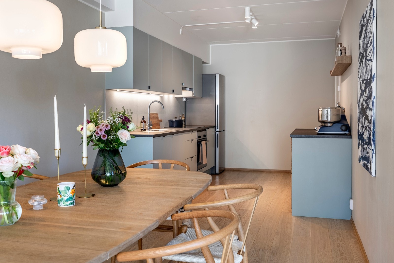 Lekkert og moderne kjøkken med slette fronter i malt utførelse og laminerte benkeplater med nedfelt oppvaskkum. Kjøkkenet er utstyrt med integrerte hvitevarer som induksjonstopp, komfyr og oppvaskmaskin, mens det er plass for kjøleskap. Galleribilde
