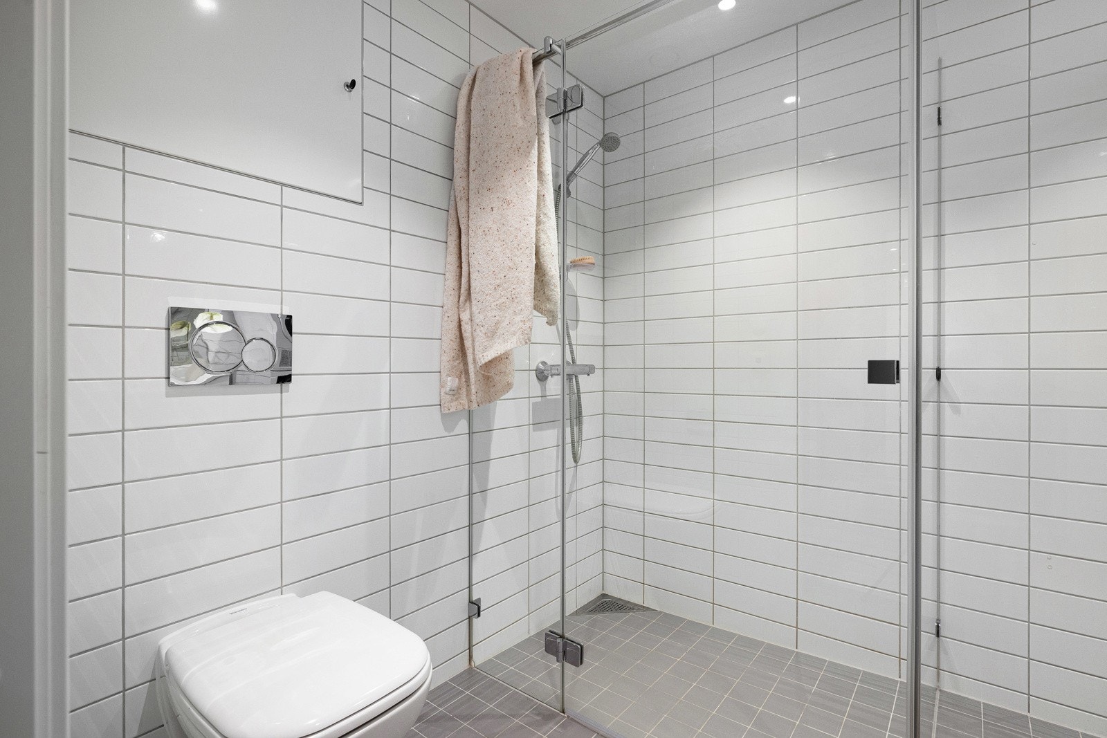 Baderomsinnredningen består av heldekkende servantskap med profilerte glatte fronter, speil over med tilhørende belysning, dusjhjørne med glassvegger og gulvmontert vegghengt toalett. Galleribilde