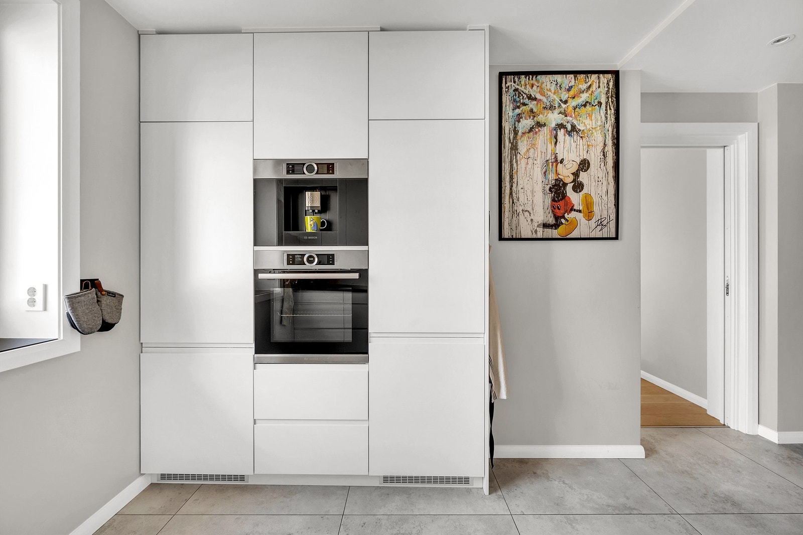 Hvitevarene er sømløst integrert i innredningen og består av kjøleskap, fryser, oppvaskmaskin, komfyr og kaffemaskin. Induksjonstopp er planlimt. Galleribilde