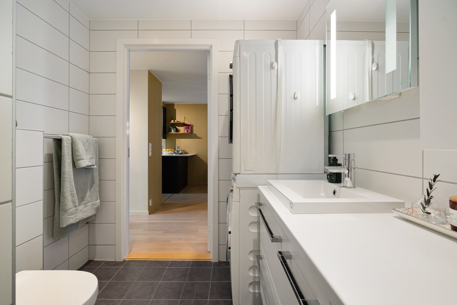 Badet er utstyrt med servant, skuffer, overskap, høyskap, speil med integrert belysning, dusj med innfellbar glassdør og vegghengt toalett. Det er også opplegg for vaskemaskin og tørketrommel Galleribilde