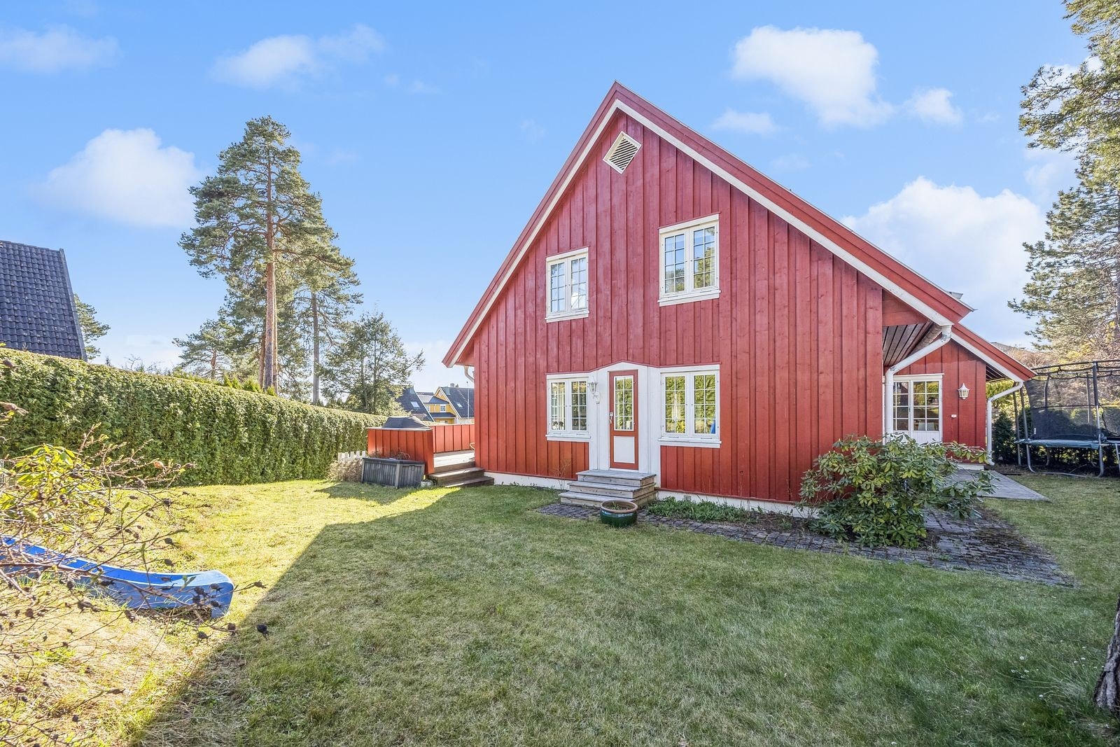 Stor grønn gressplen opparbeidet med beplantning, sklie og trampoline for barna. Galleribilde