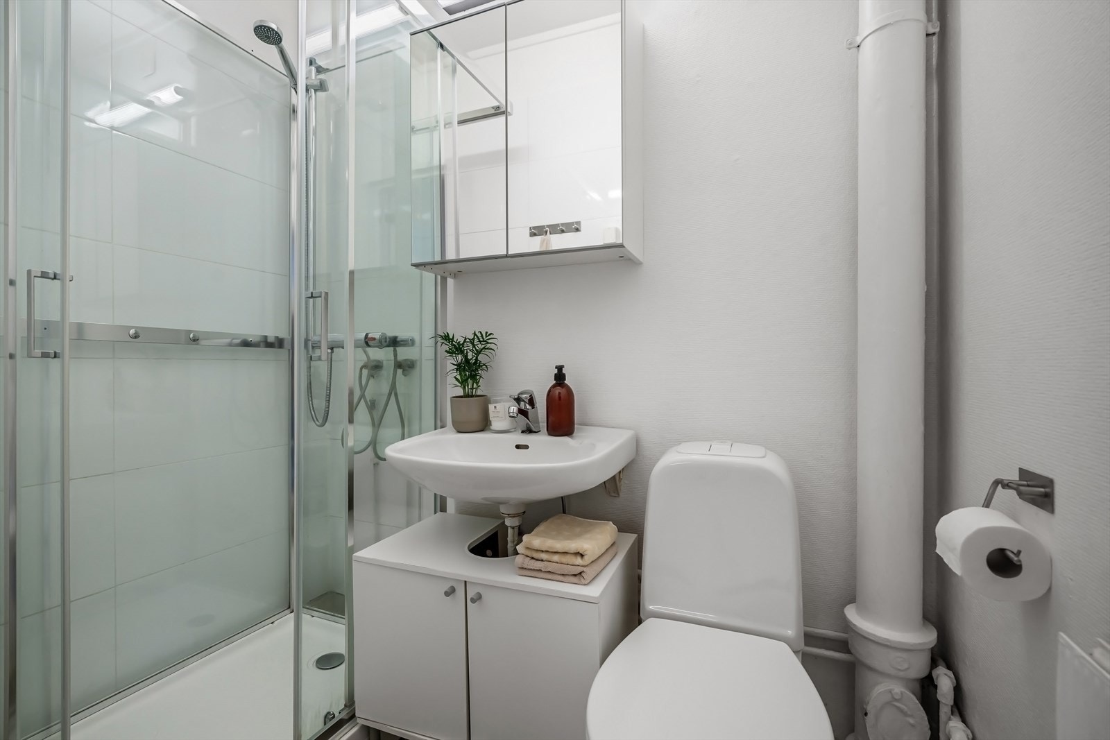 Bad med dusj, toalett, servant, skap og speilskap. Galleribilde