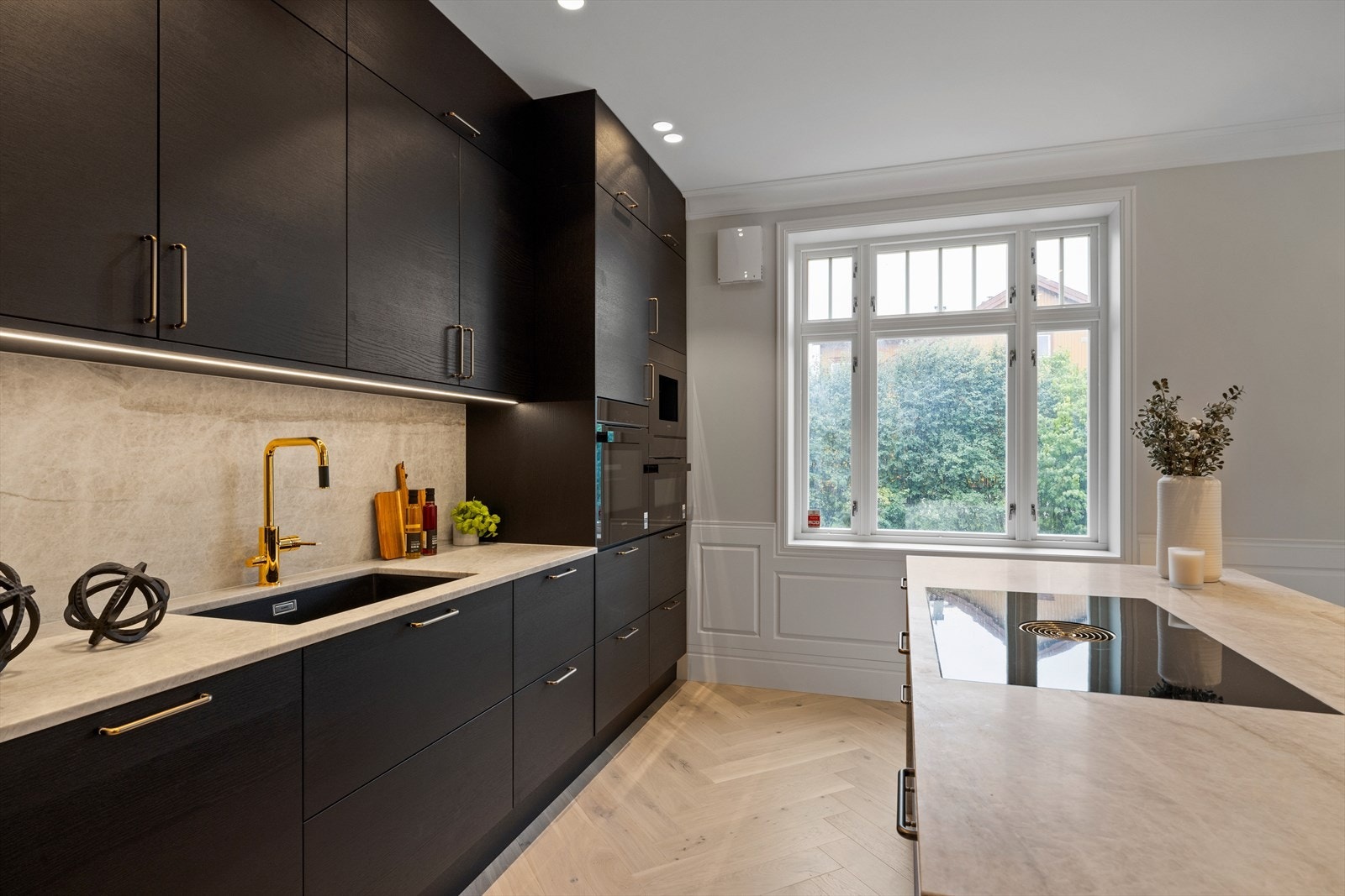 Mørke glatte fronter på skuffer og skap. Benkeplater og bakplate på vegg (splash plate) i lys stein. Underlimt oppvaskkum i sort kompositt Galleribilde