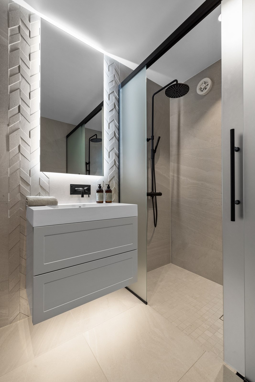 Det delikate badet er innredet med nedfelt servant, veggmontert toalett og dusjvegger/hjørne. Flislagt gulv med fall på hovedgulv mot sluk. Nedsenket gulv i dusjnisje med fall til sluk. Flislagte vegger og malt himling med innfelte downlights Galleribilde