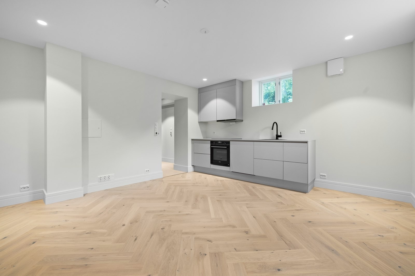 Stue/kjøkken med ny kjøkkeninnredning med hvite glatte fronter på skuffer og skap. Benkeplate i hvit laminat med nedfelt oppvaskkum i sort kompositt Galleribilde