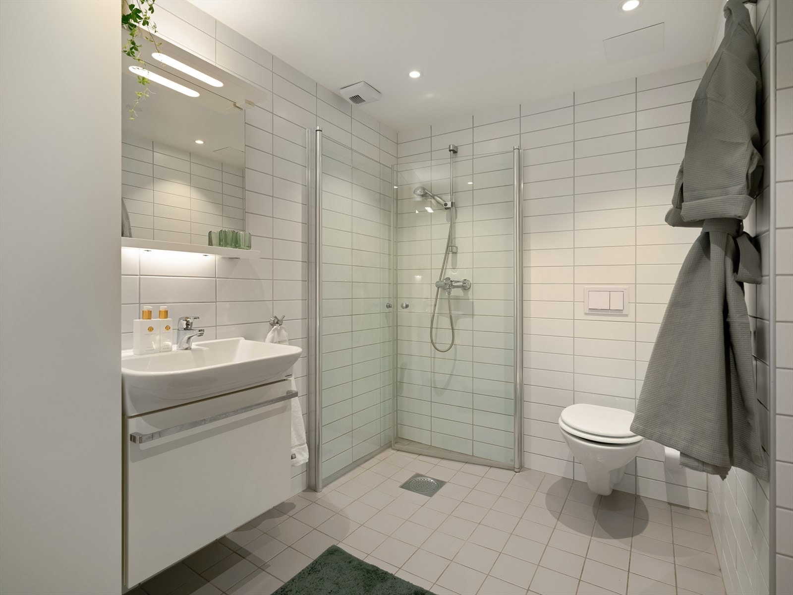 Baderomsinnredning med servant på underskap med speil og belysning over samt langskap på siden som gir godt med oppbevaringsplass. Galleribilde