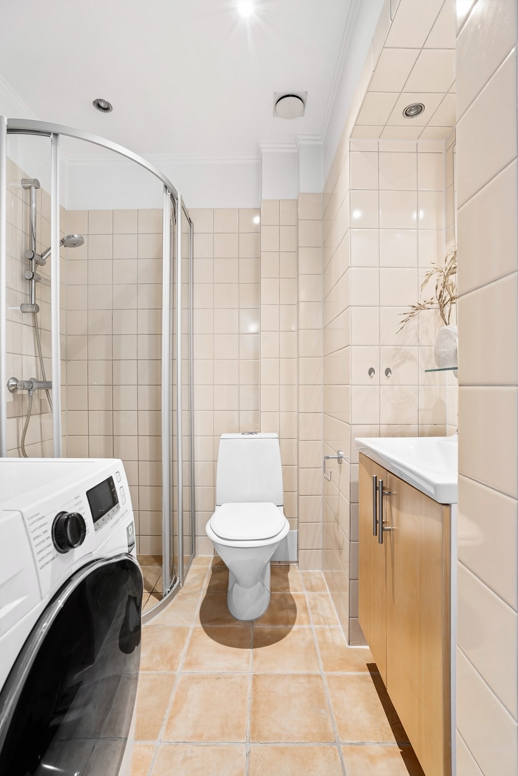 Baderom har flislagt gulv med gulvvarme, flislagte vegger og nedsenket himling med downlights. Videre er det dusjhjørne med plassmontert skinne og skyvedører i glass med vegghengt dusjarmatur. Galleribilde