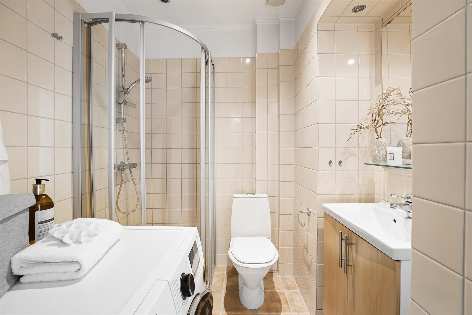 Baderom med opplegg for vaskemaskin, vegghengt servant innredning med dører, ovenpåliggende servant med ett-greps armatur, speil og gulvstående toalett. Galleribilde