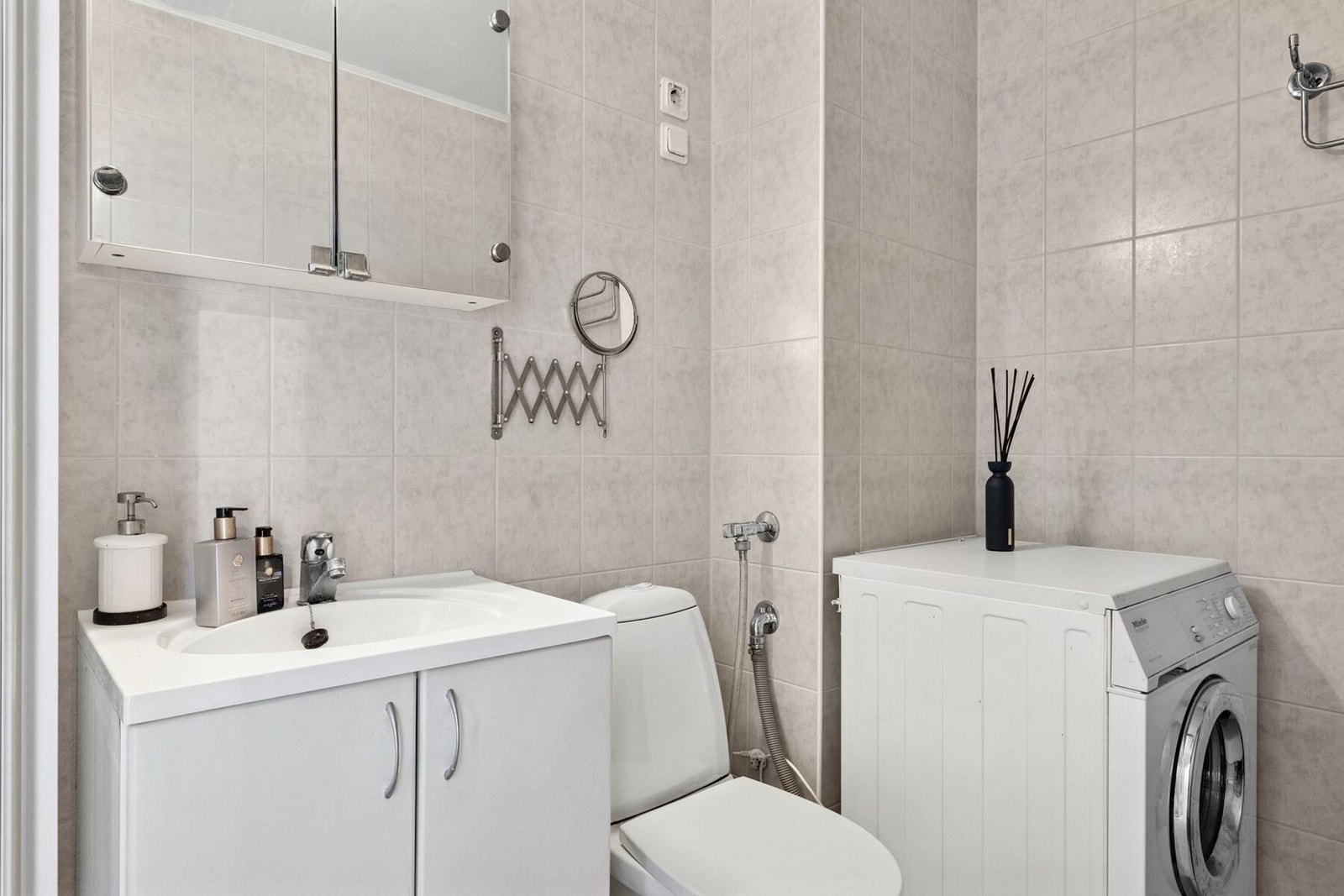 Videre kommer vi til badet. Badet er innredet med lyse fliser og har plass til både vaskemaskin og praktisk baderomsinnredning. Galleribilde