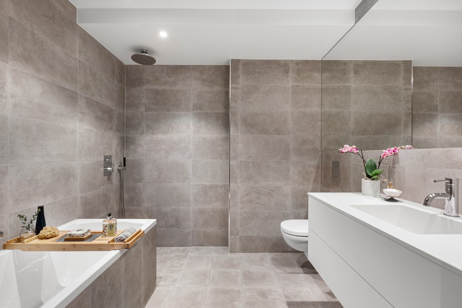 Badet i første etasje ligger i suiteløsning med hovedsoverommet, og har samme moderne og gjennomførte stil som det andre badet - med store fliser, vegghengt toalett, regnfallsdusj og innfliset badekar. Galleribilde