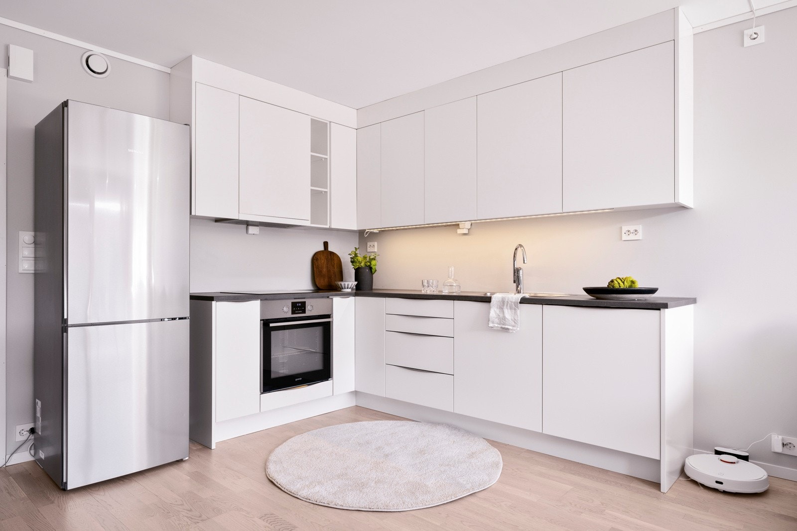 Kjøkkenet er arealeffektivt og moderne, med hvite fronter, takhøye skap og koksgrå laminatbenkeplate med nedfelt kum i stål. Galleribilde