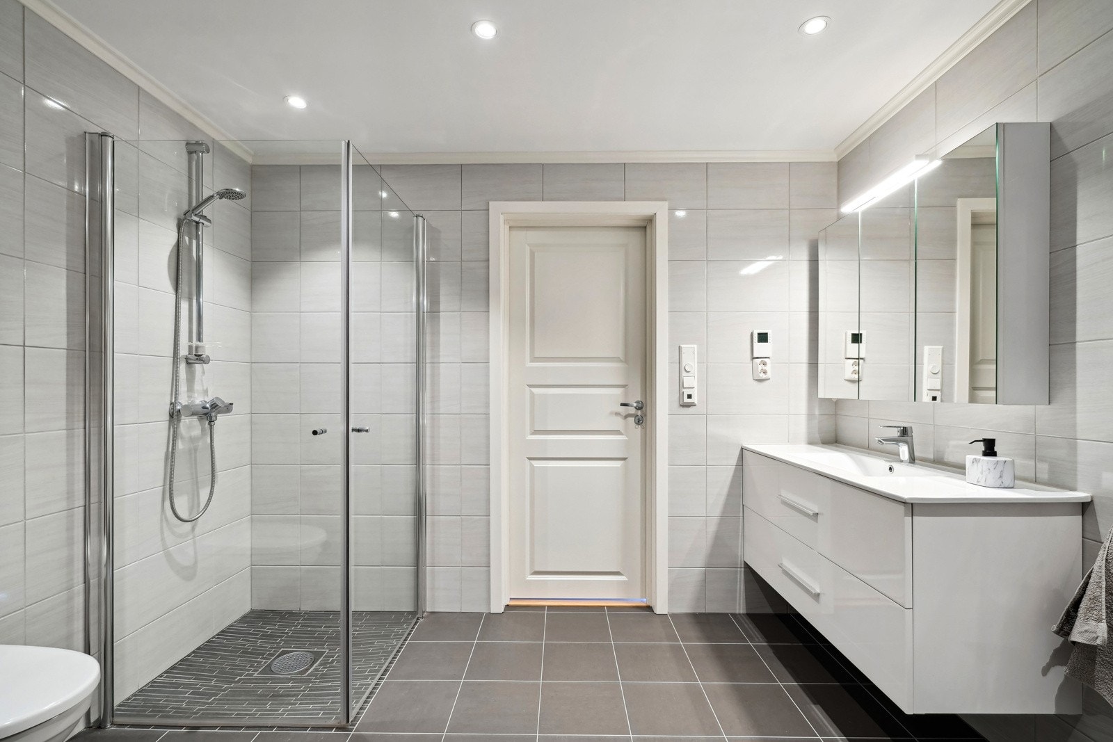 Pent flislagt baderom med innredning, vegghengt wc, dusjvegger og opplegg for vaskemaskin. Galleribilde