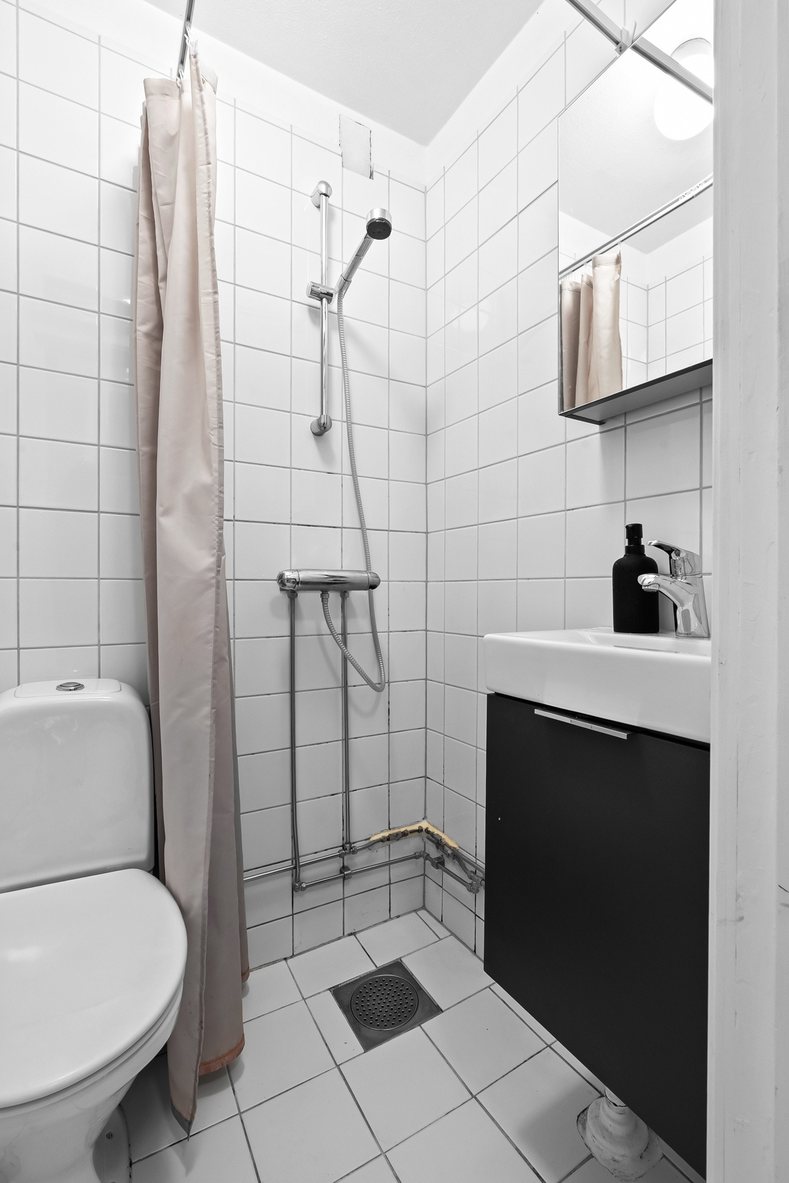 Flislagte flater, dusjnisje og oppbevaringsplass i form av speil- og servantskap Galleribilde