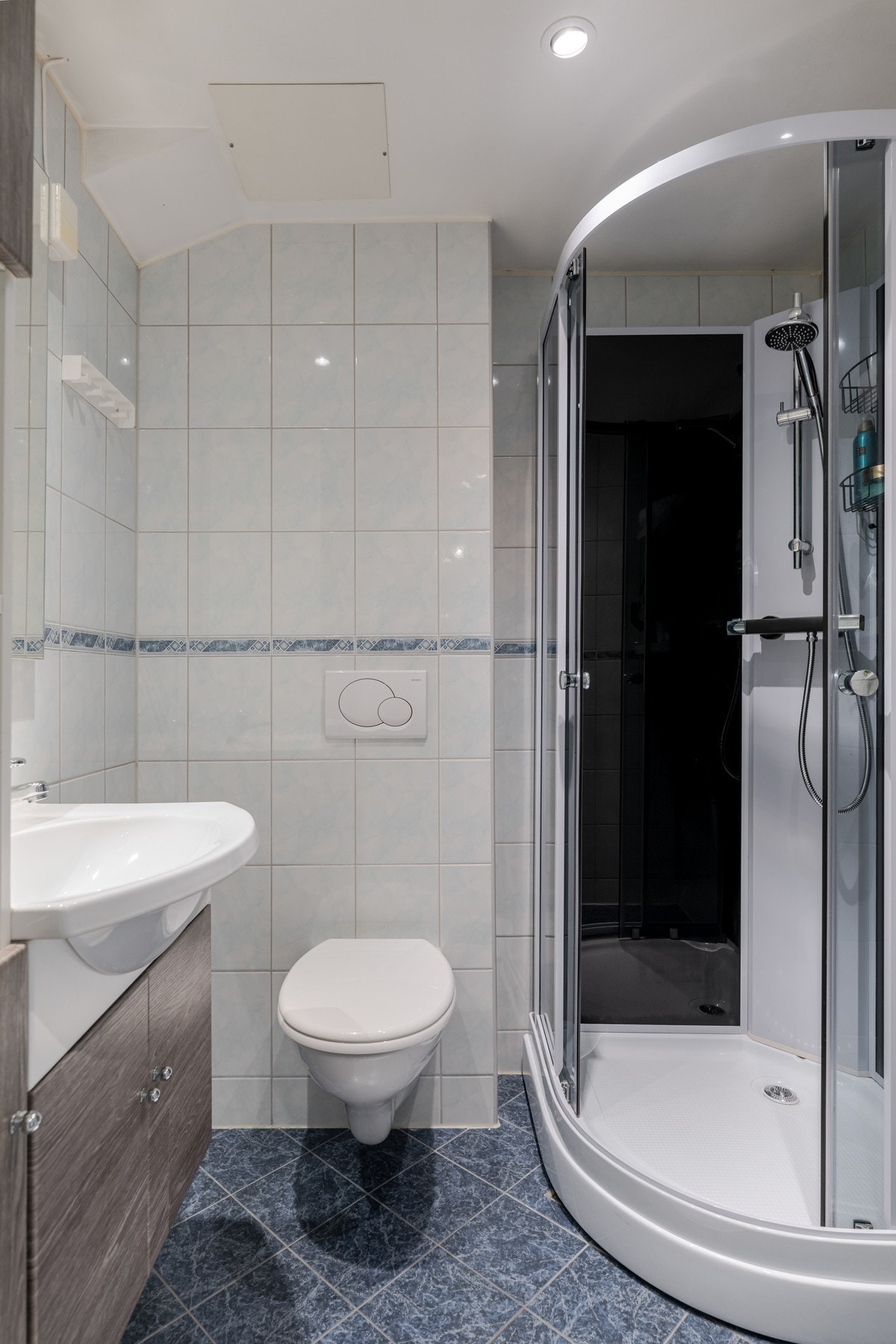 Badet har innredning med servant, veggmontert toalett og dusjkabinett. Galleribilde